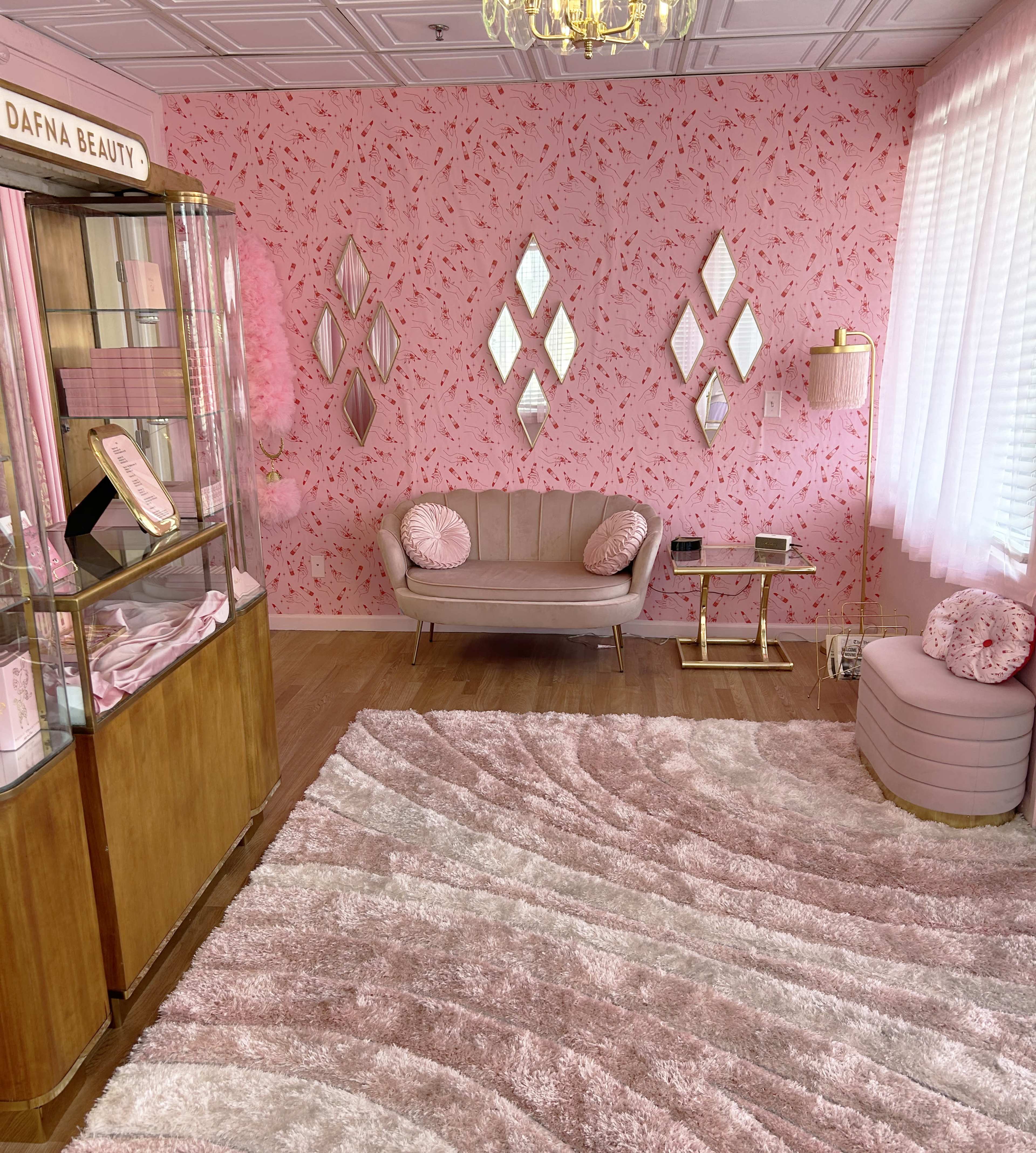 A pink-themed boutique interior with floral wallpaper, a plush seating area, a display case, and a large, textured rug.