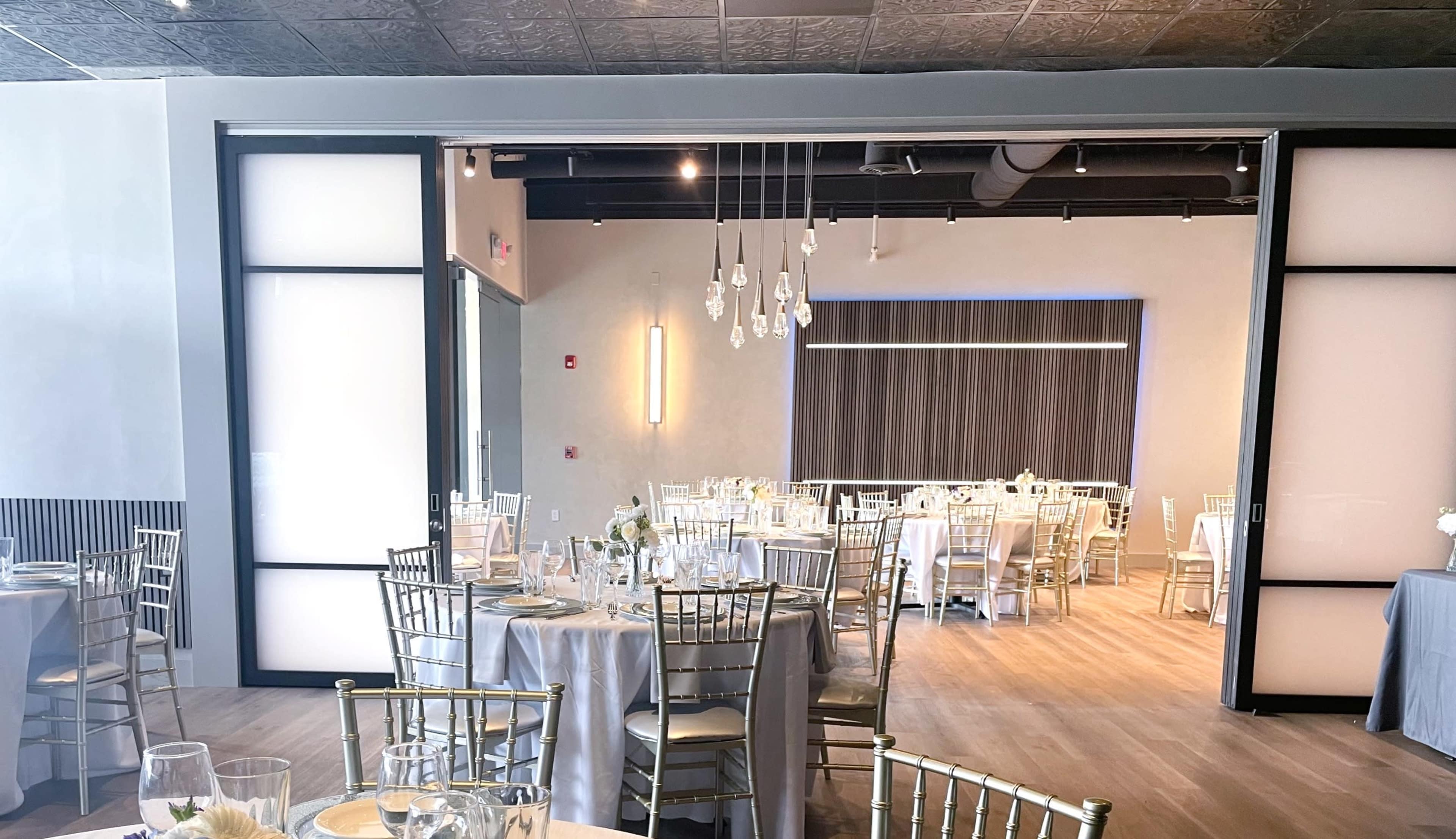 A modern dining hall set with round tables and elegant chairs, bathed in natural light from large windows.
