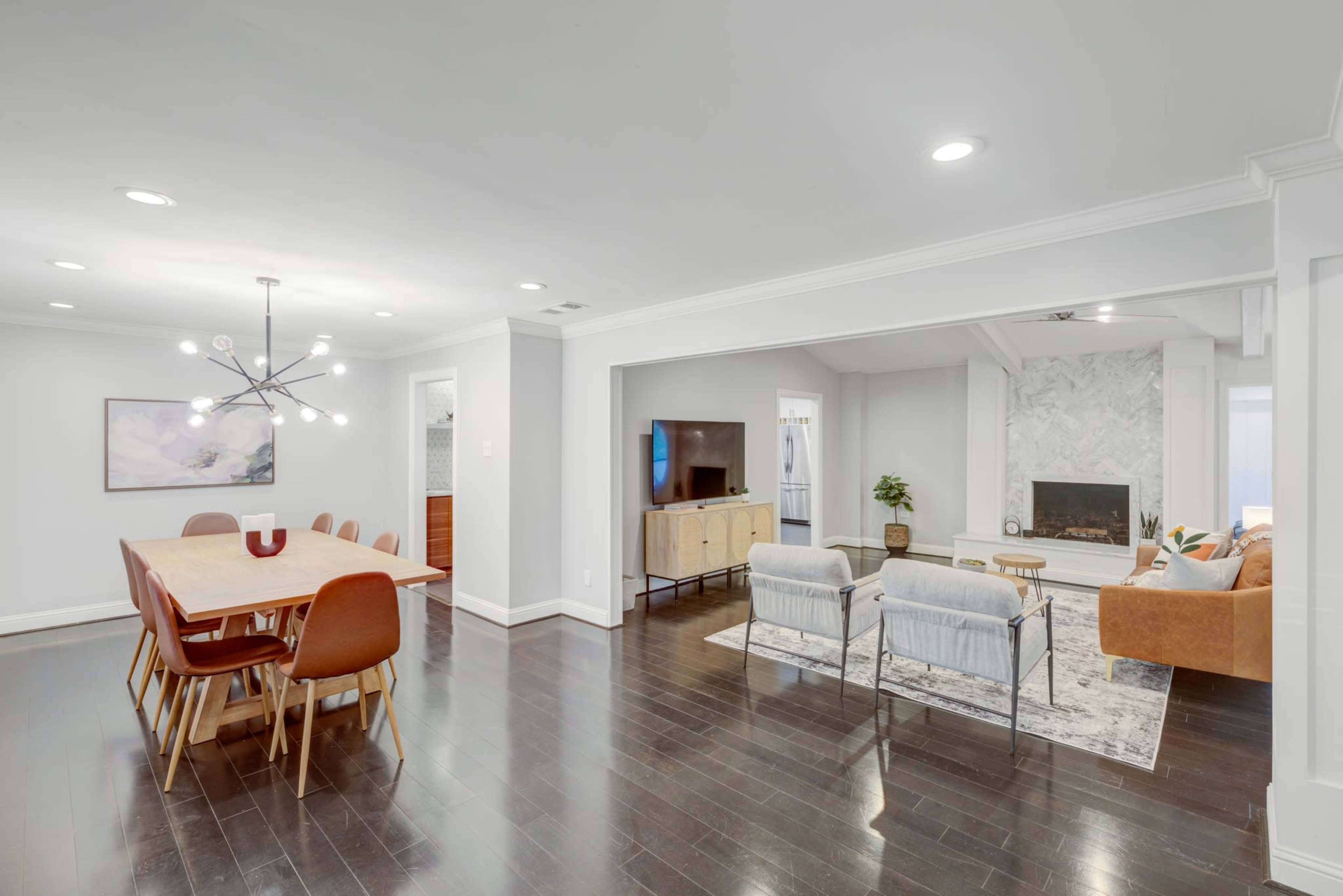 The image shows a modern, open-concept living and dining area with a wooden dining table, a cozy seating arrangement, and a fireplace.