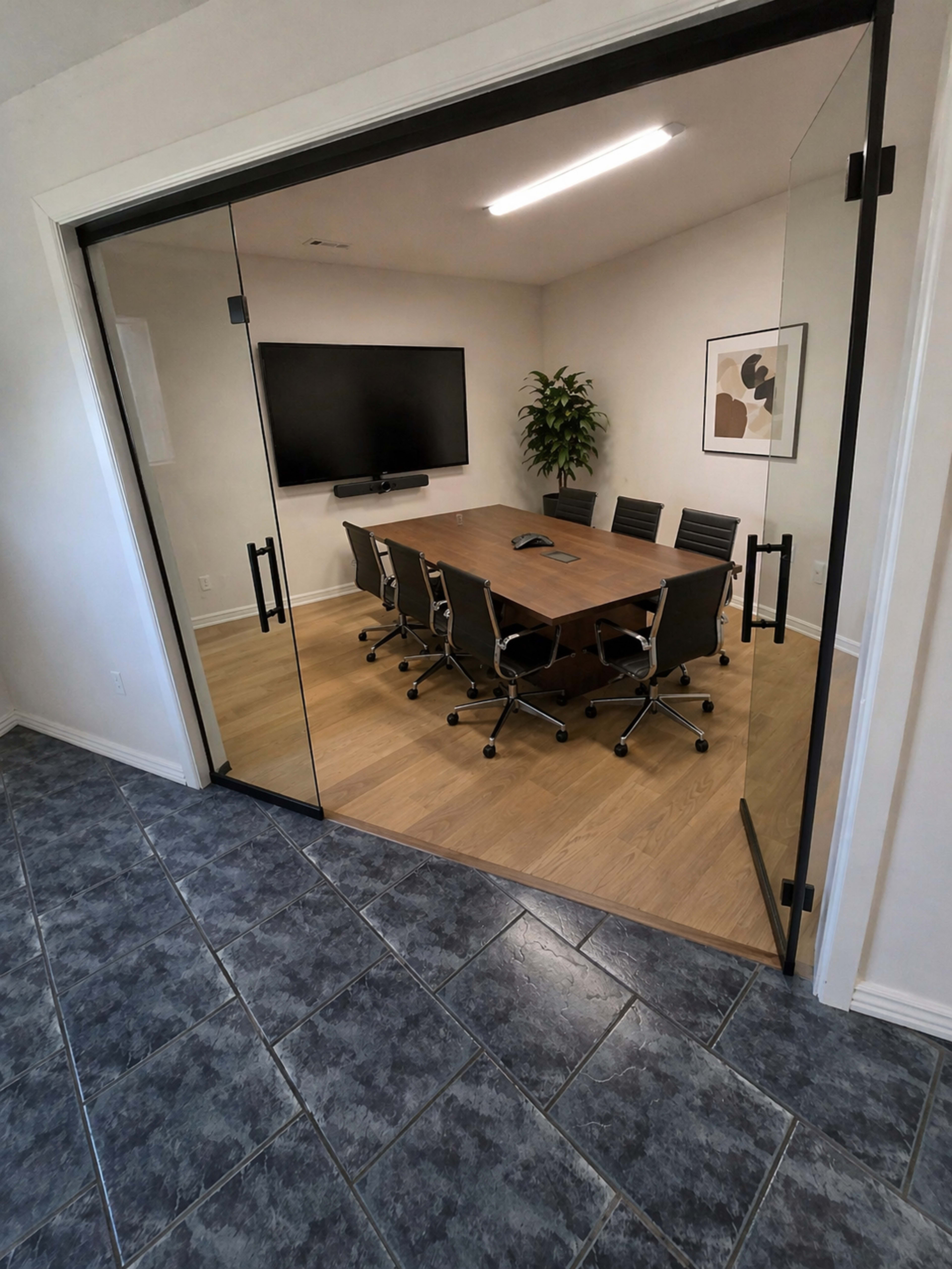 A modern conference room is visible through glass doors, featuring a large table surrounded by black chairs and equipped with a wall-mounted screen.