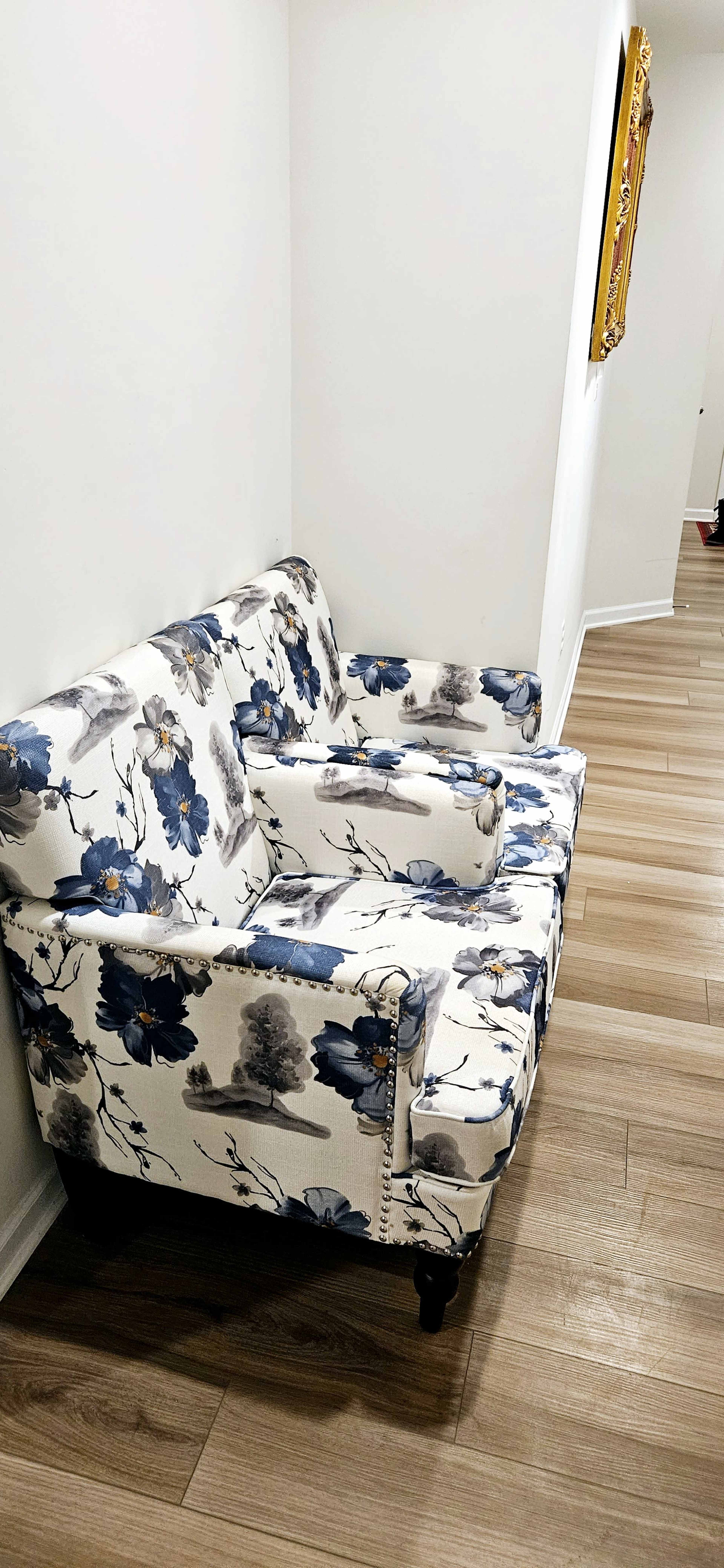 A floral-patterned loveseat is positioned against a white wall in a room with wooden floors.