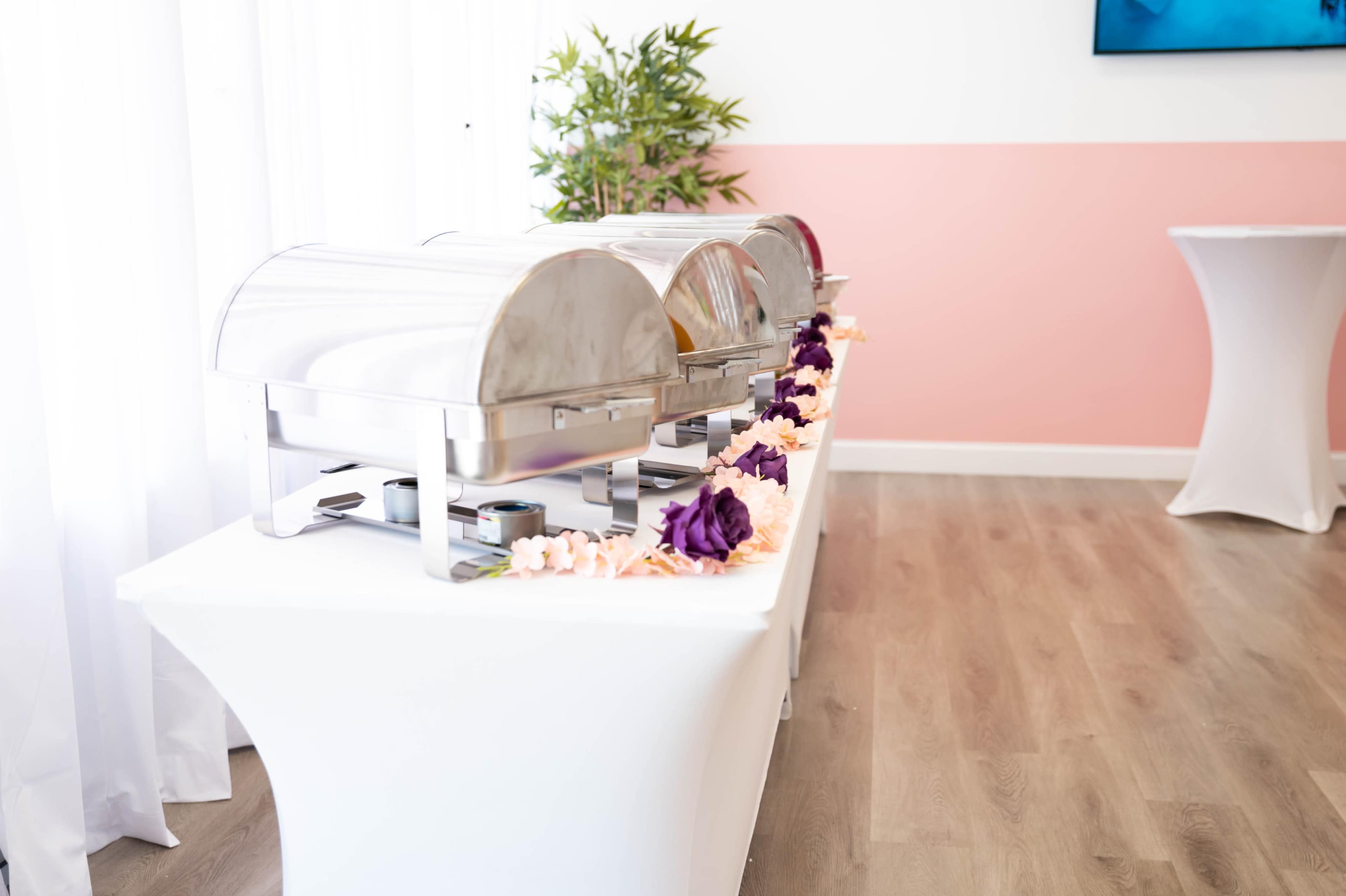 A catering display features three covered food warmers arranged on a table adorned with floral decorations.