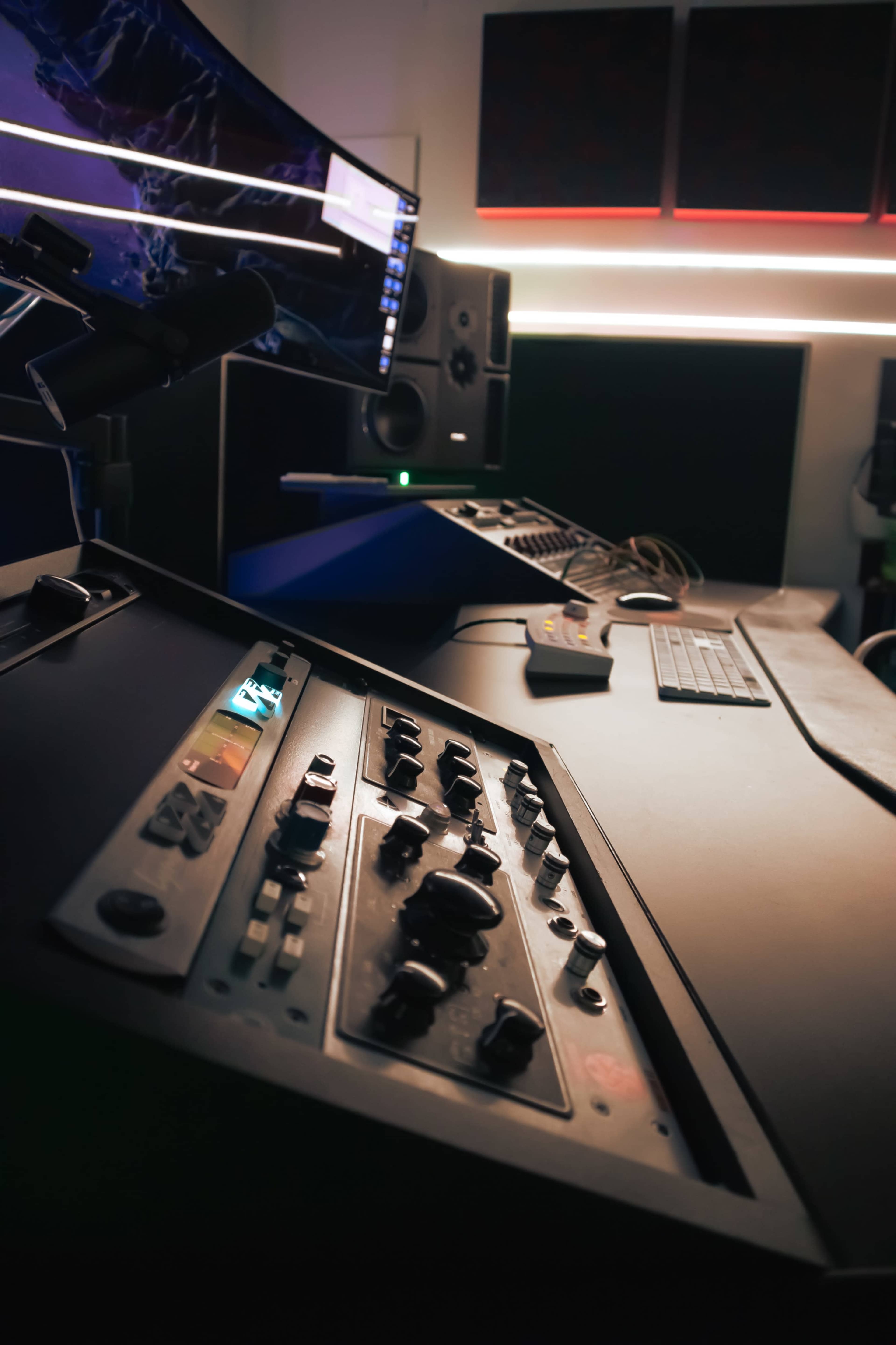 The image shows a close-up of a music production workspace featuring mixing equipment, a computer monitor, studio speakers, and a keyboard.