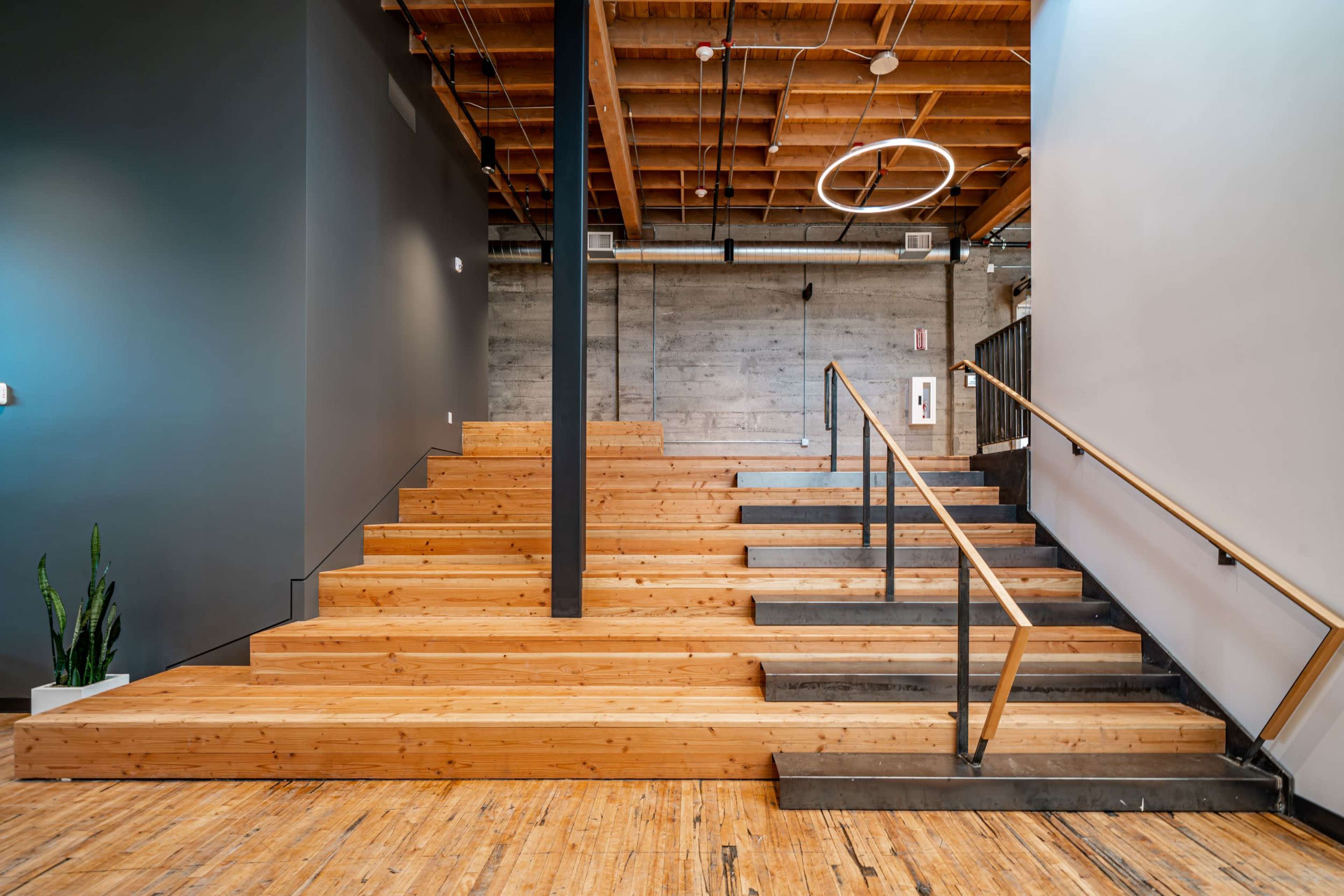 A set of wooden stairs leading up to a minimalist interior space with exposed beams and a modern railing.