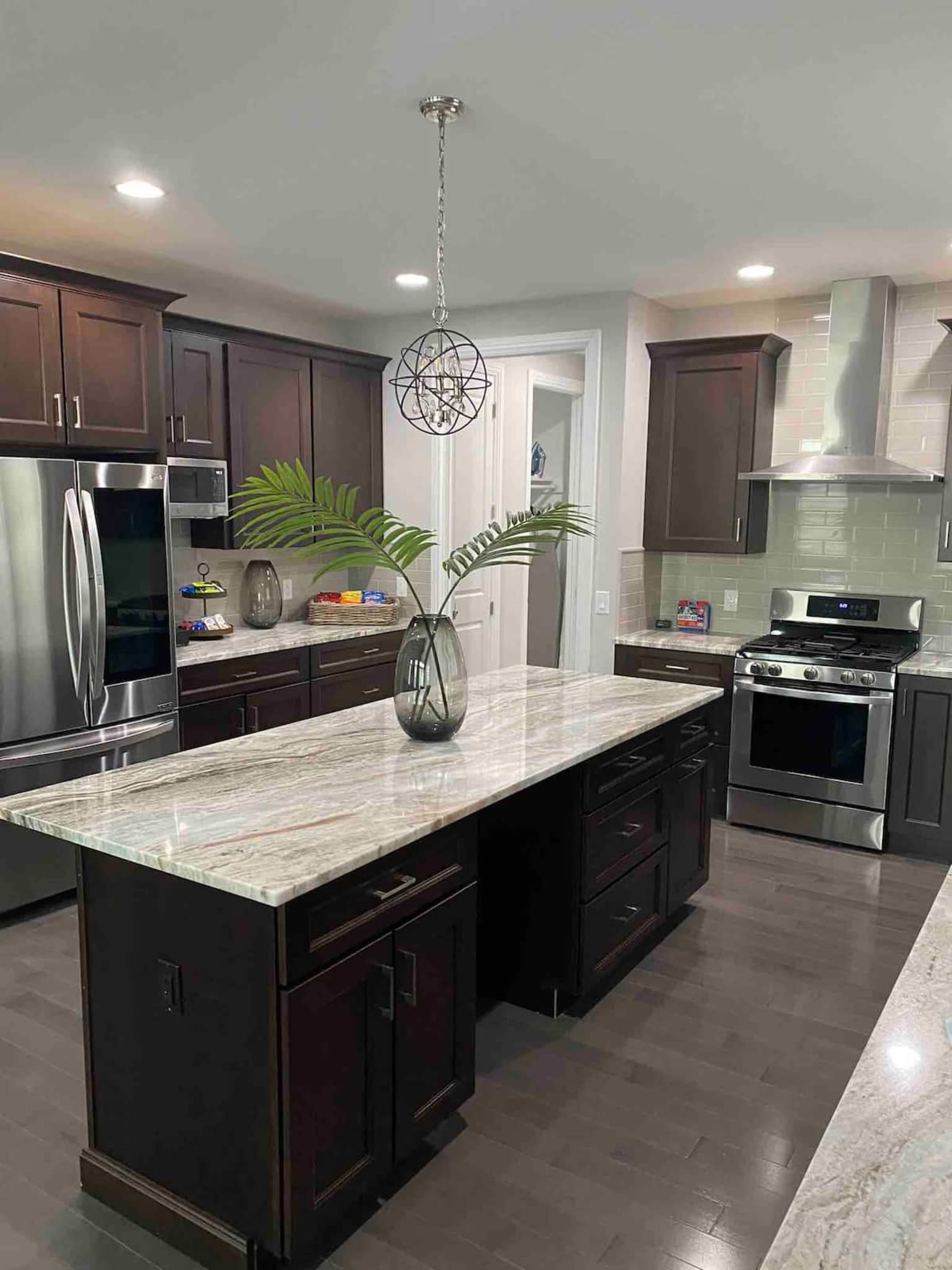 A modern kitchen features dark wooden cabinets, a large island with a marble countertop, and stainless steel appliances.