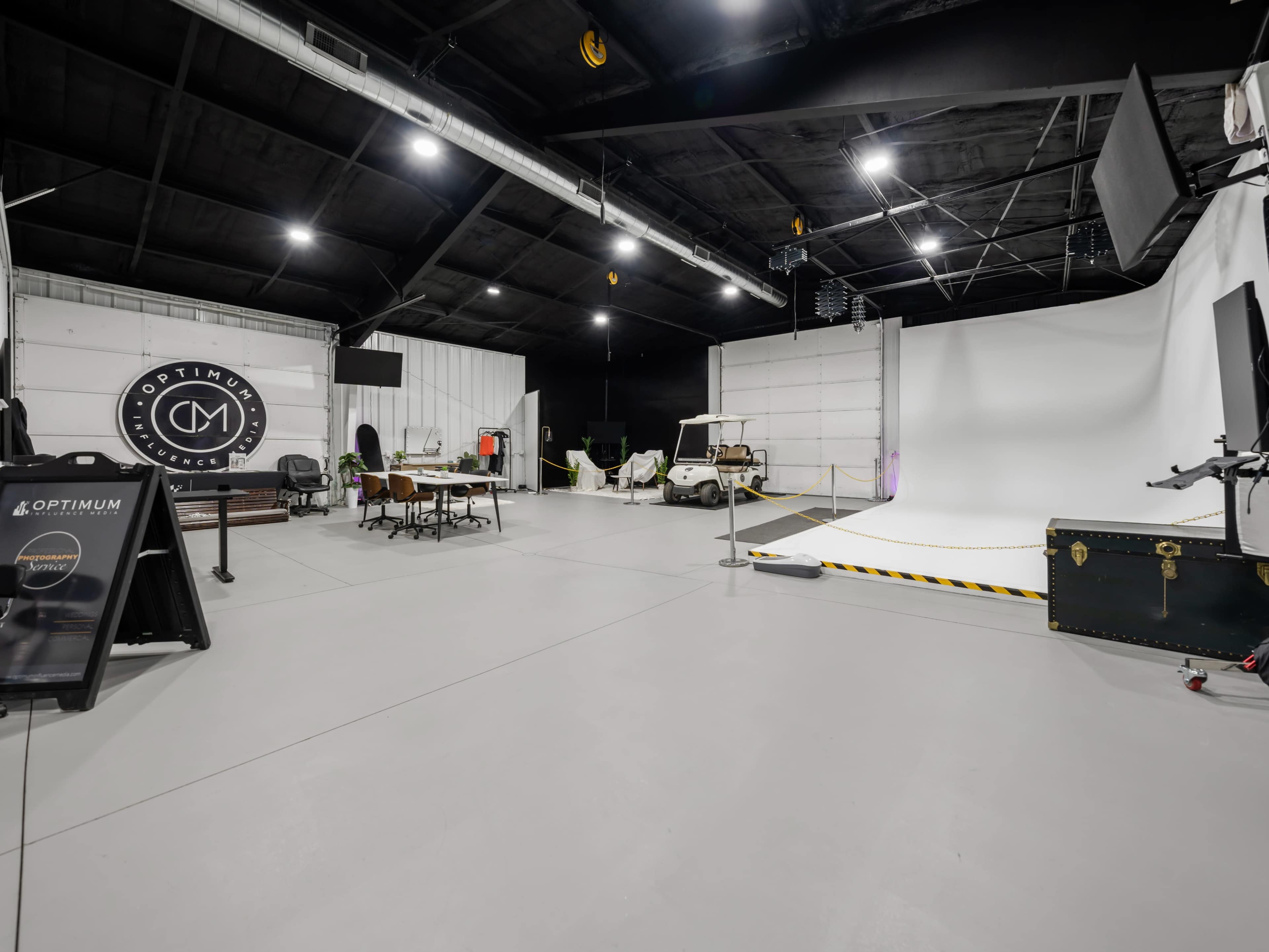 A spacious indoor studio with a white backdrop, several tables and chairs, a golf cart, and various equipment arranged around the area.
