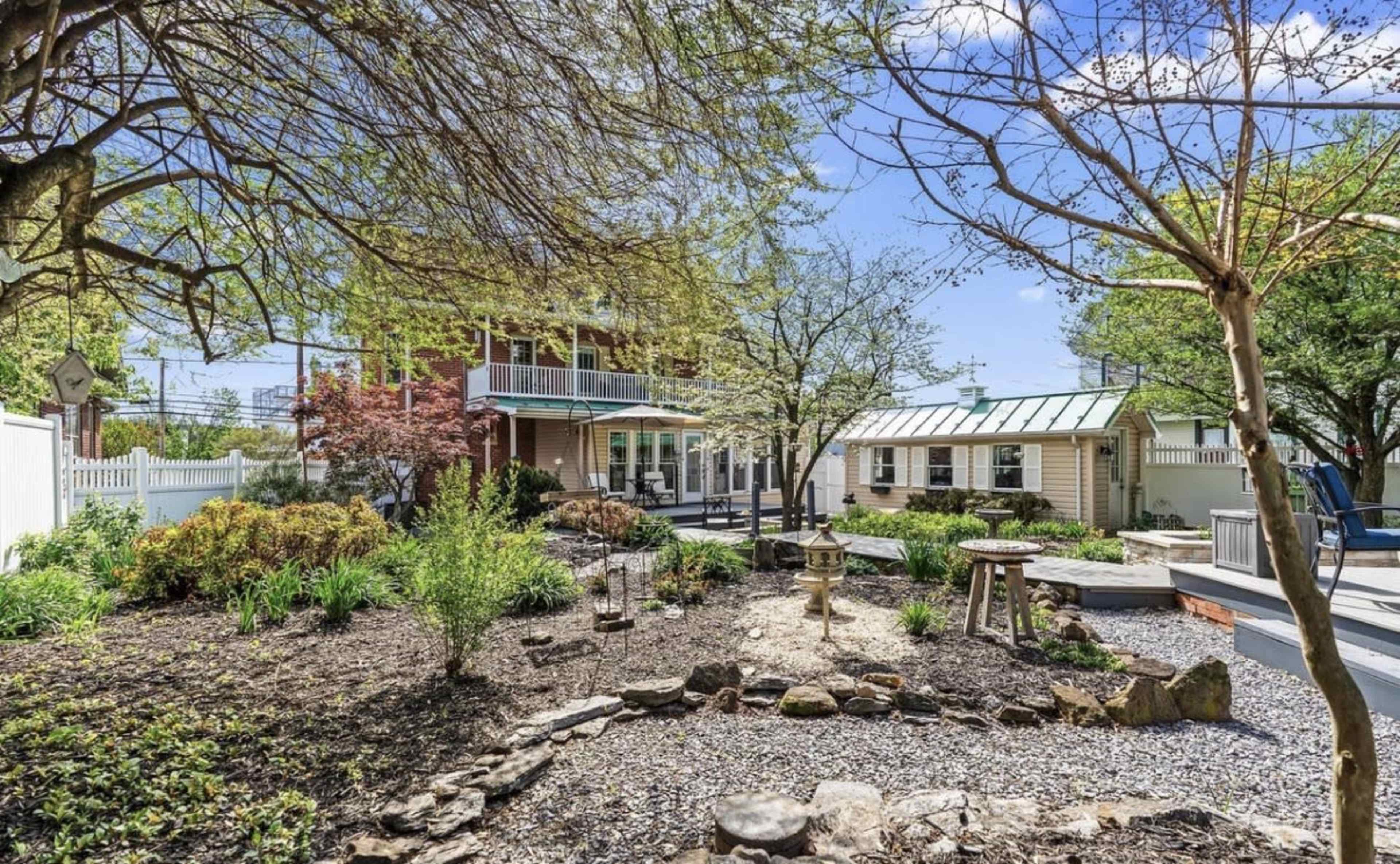 The image shows a landscaped yard with various plants, a stone path, and a two-story house in the background.