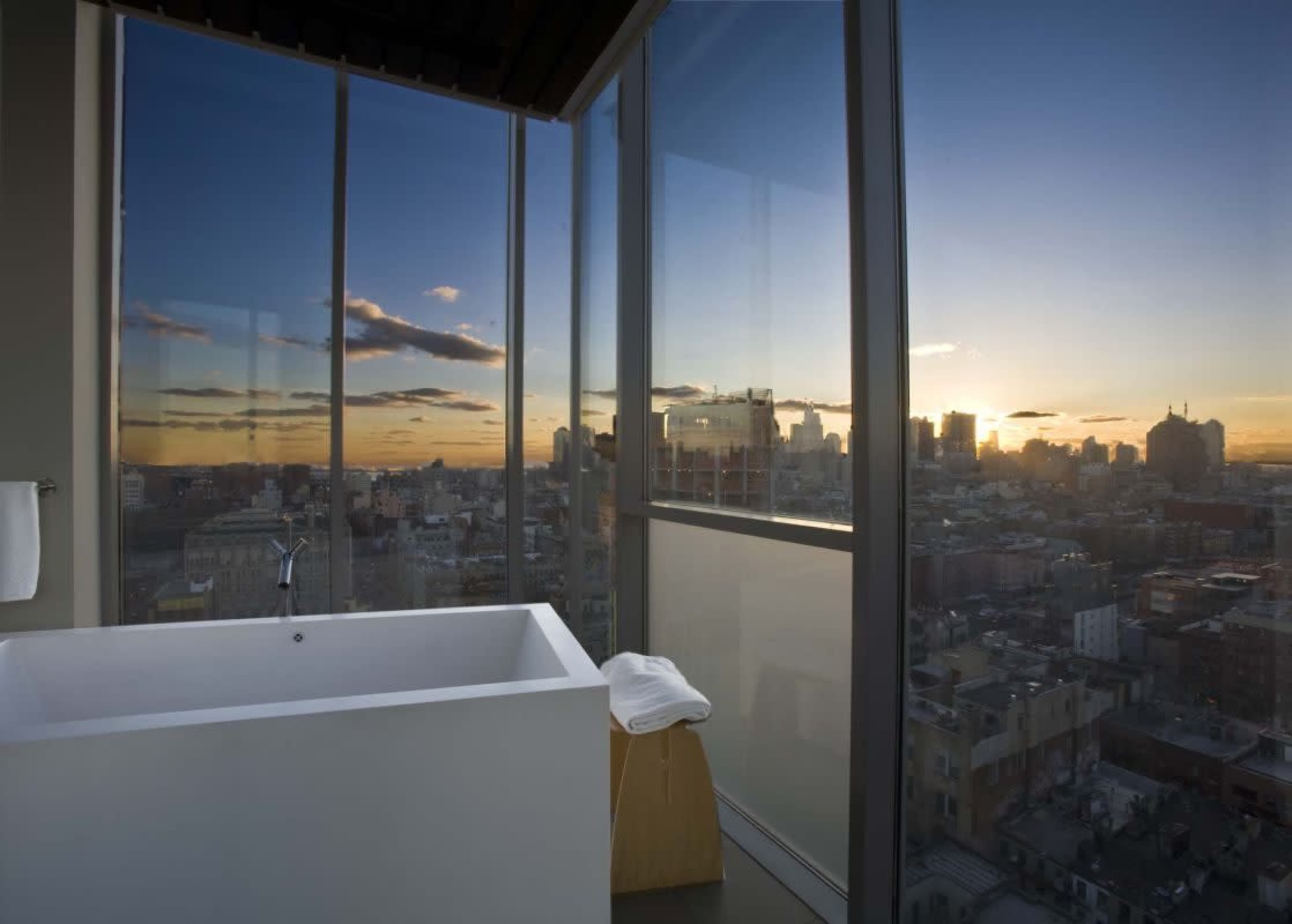 A modern bathroom features a freestanding tub beside large windows showcasing a city skyline at sunset.