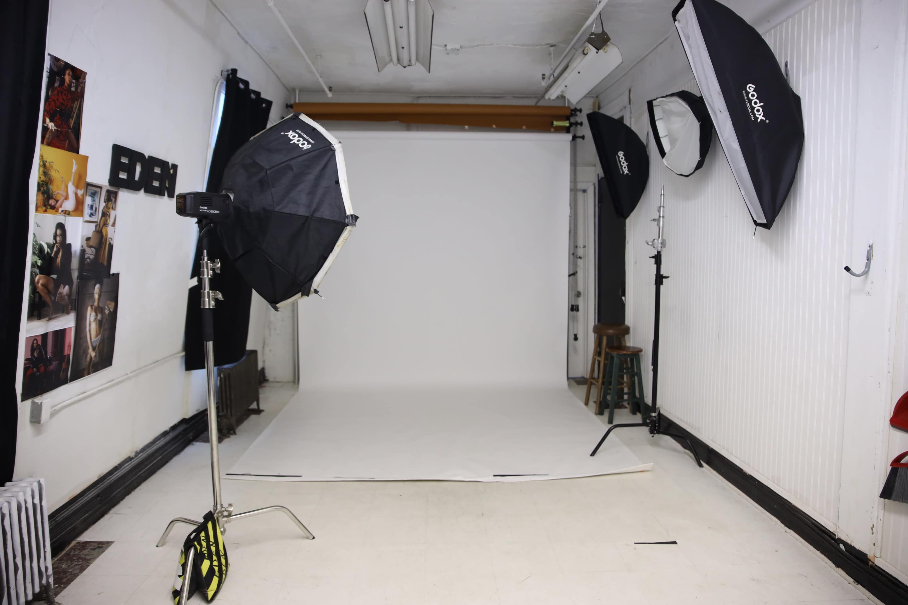 A photography studio with a white backdrop, lighting equipment, and various props arranged along the walls.