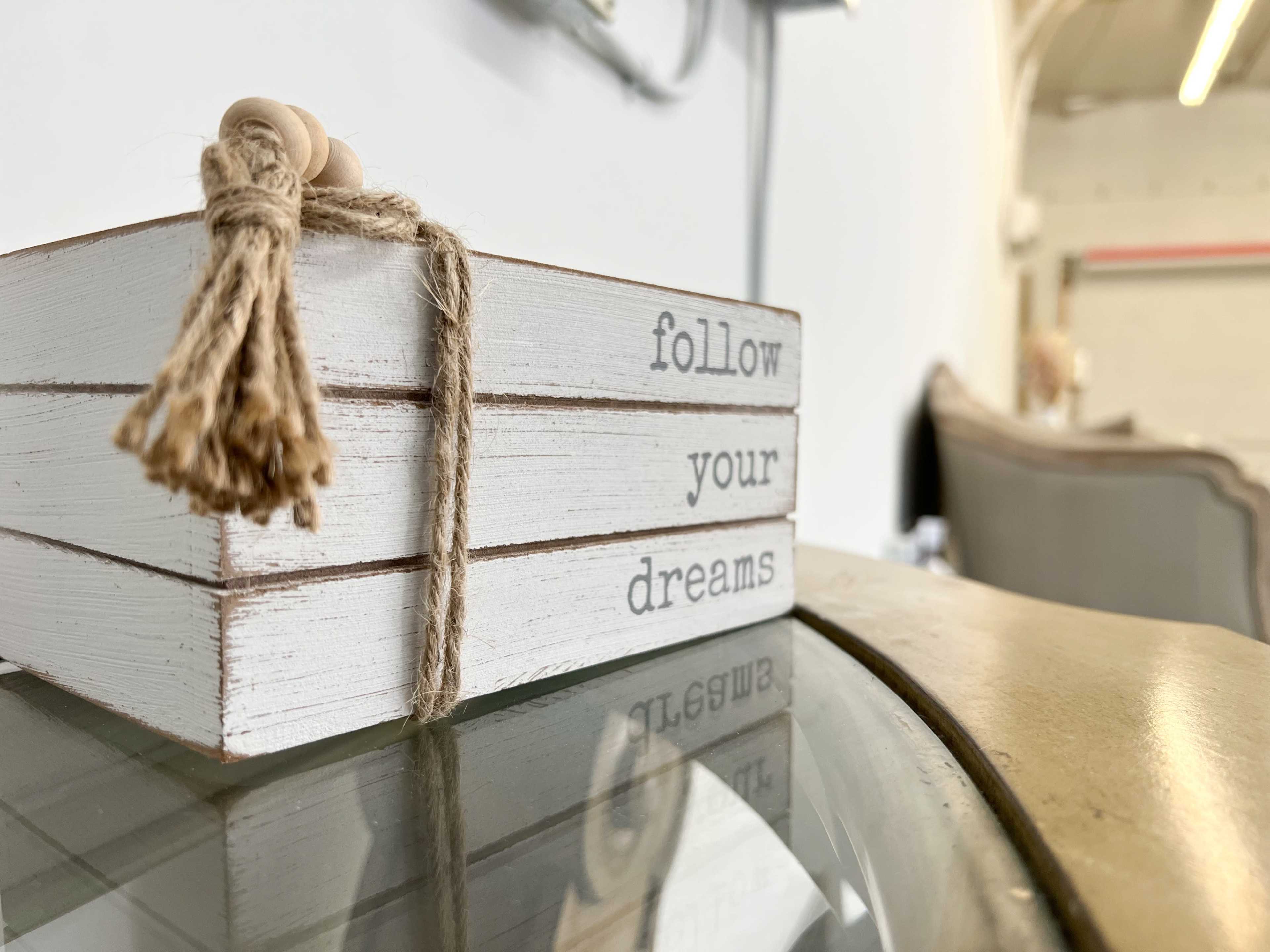 A small wooden box with the phrase "follow your dreams" is placed on a glass surface.