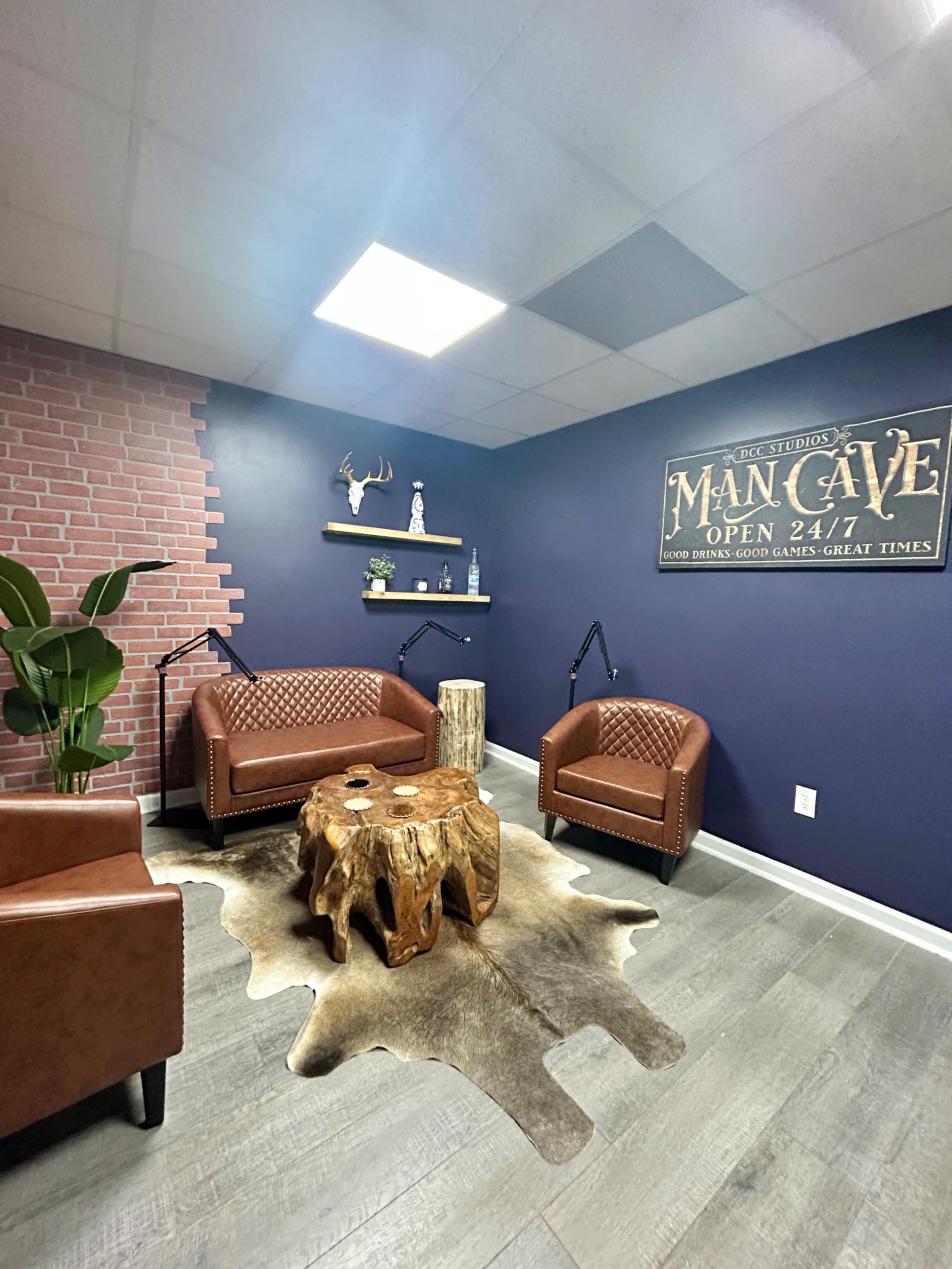 The image shows a cozy room featuring two brown leather sofas, a rustic wooden coffee table, a cowhide rug, and a wall adorned with a vintage sign that reads "Man Cave."
