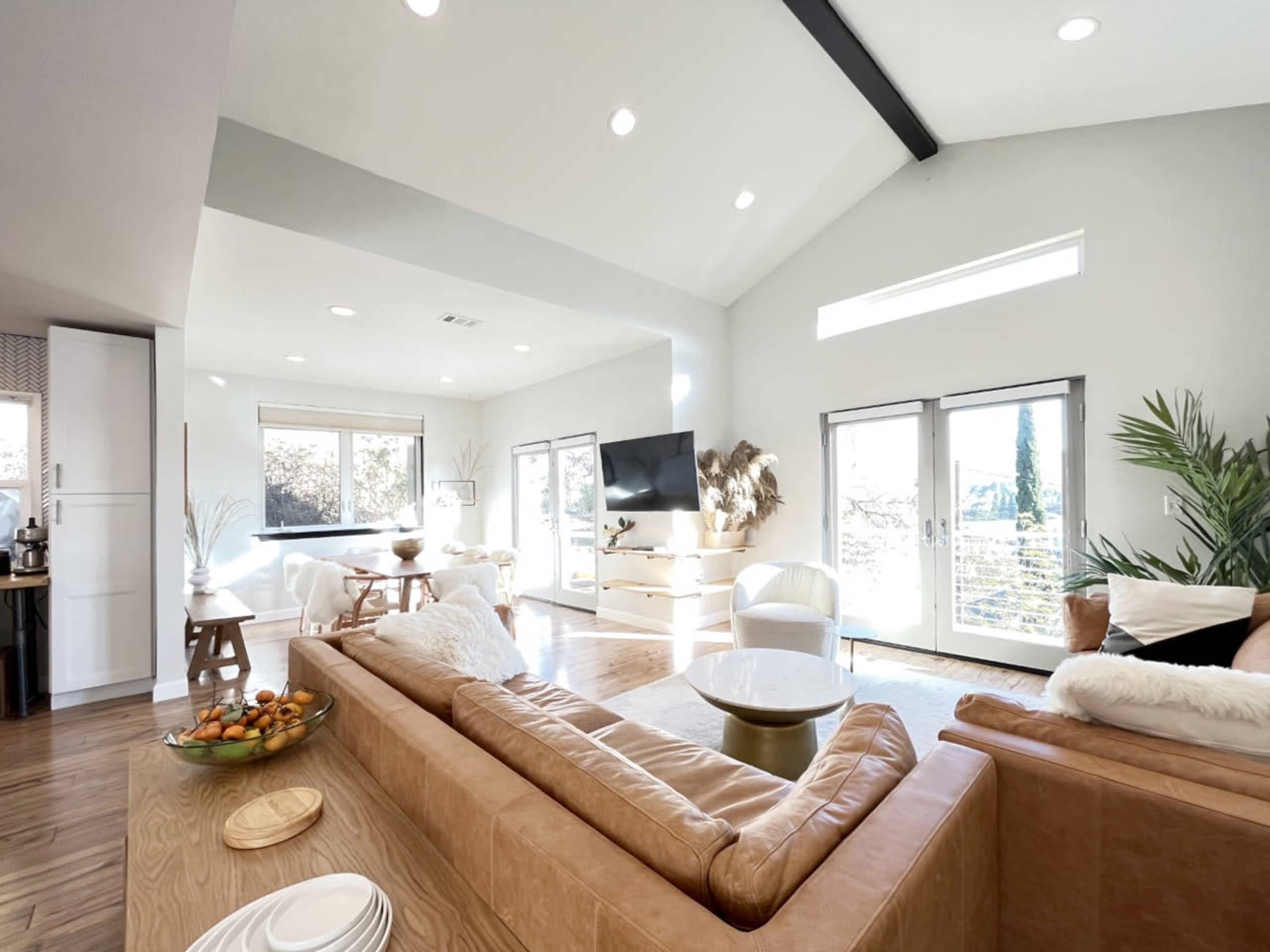 A modern living room with large windows, a comfortable leather sofa, and a coffee table, all arranged in an open space with high ceilings.
