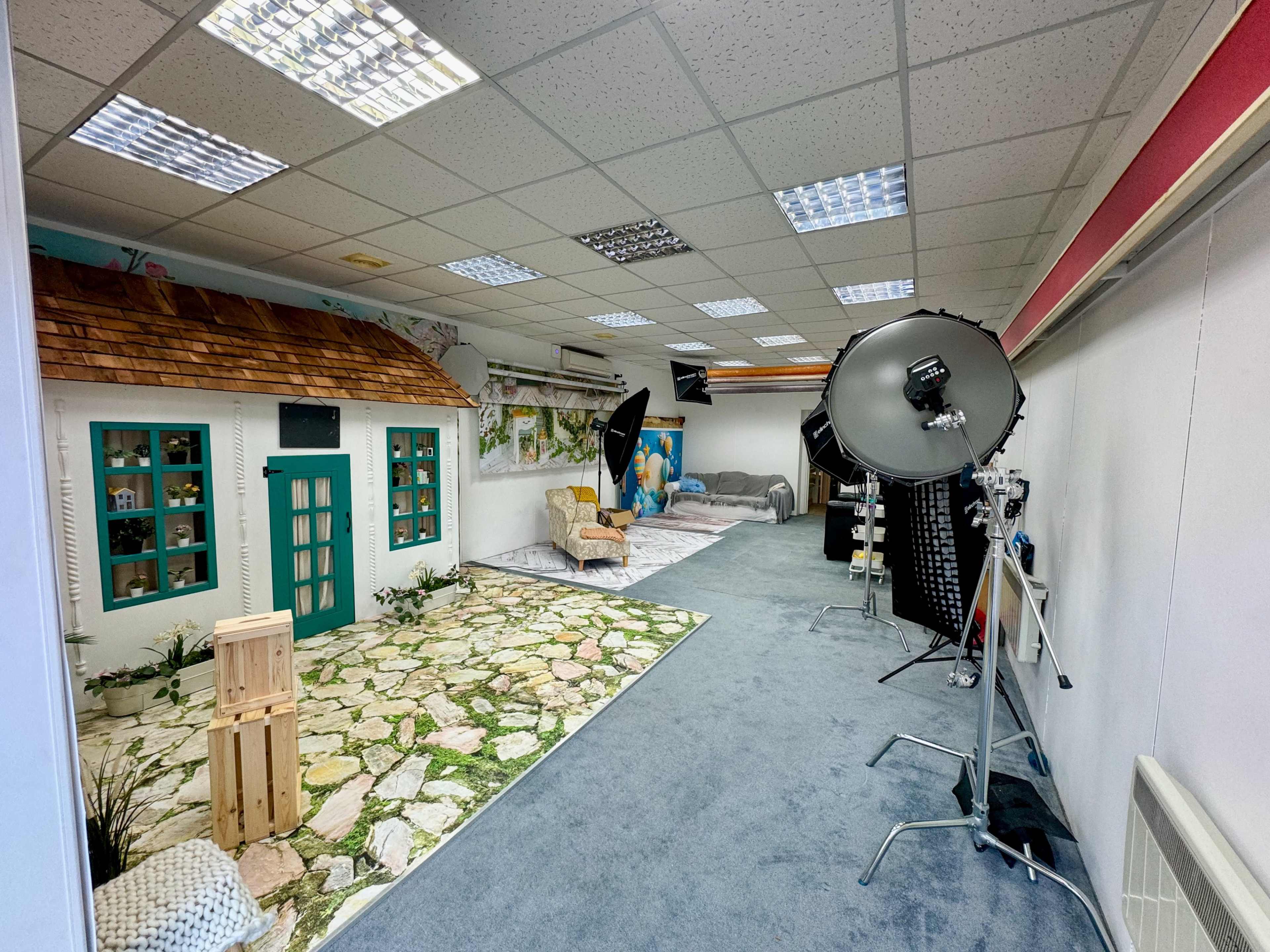 A photography studio featuring a faux cottage interior with a stone pathway and multiple lighting setups.