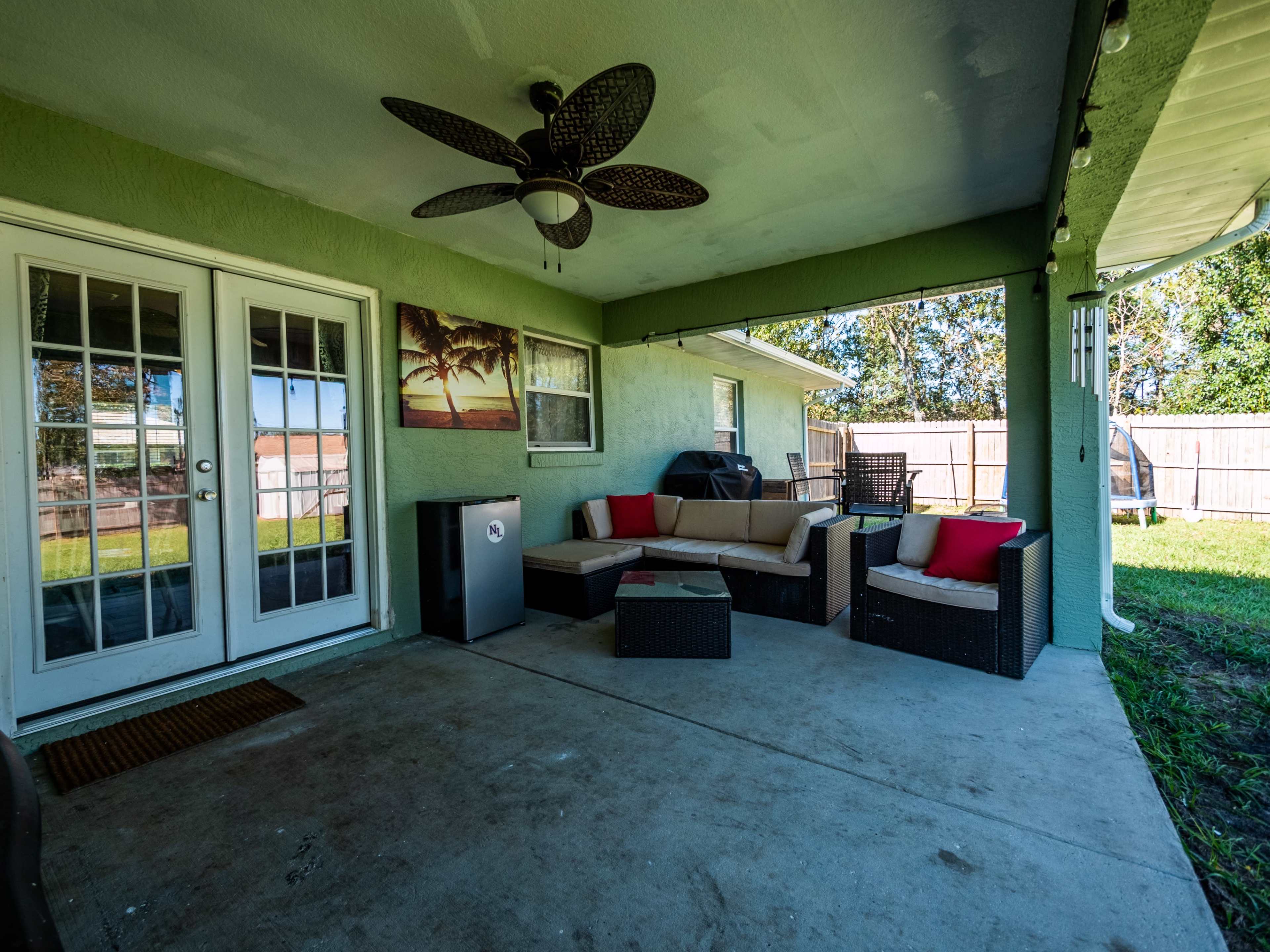 A covered patio with a seating area featuring a couch and chairs, a grill in the corner, and double doors leading to the interior of a house.