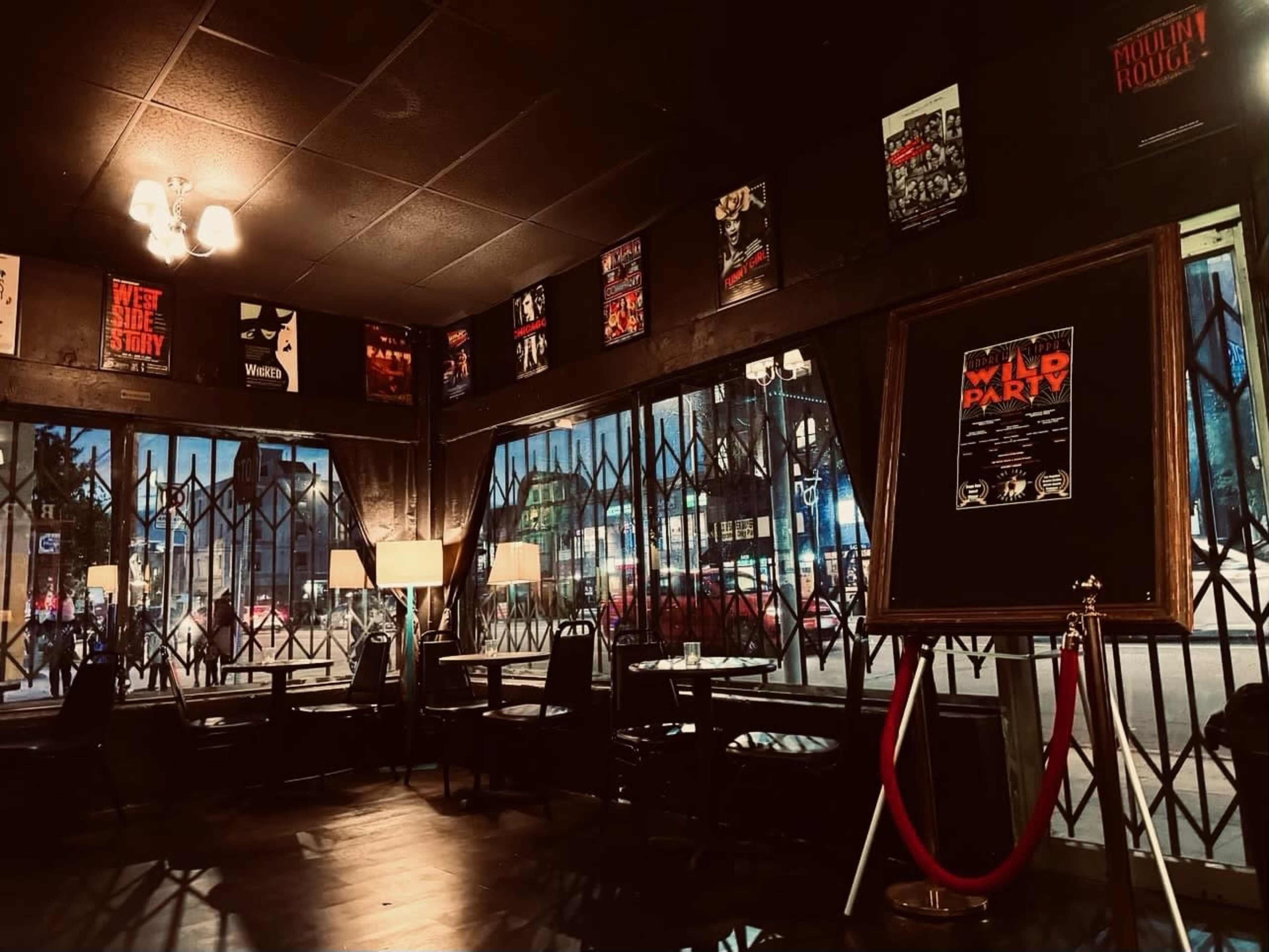 The image shows a dimly lit café with black walls, framed posters on the walls, and large windows displaying a city street outside.