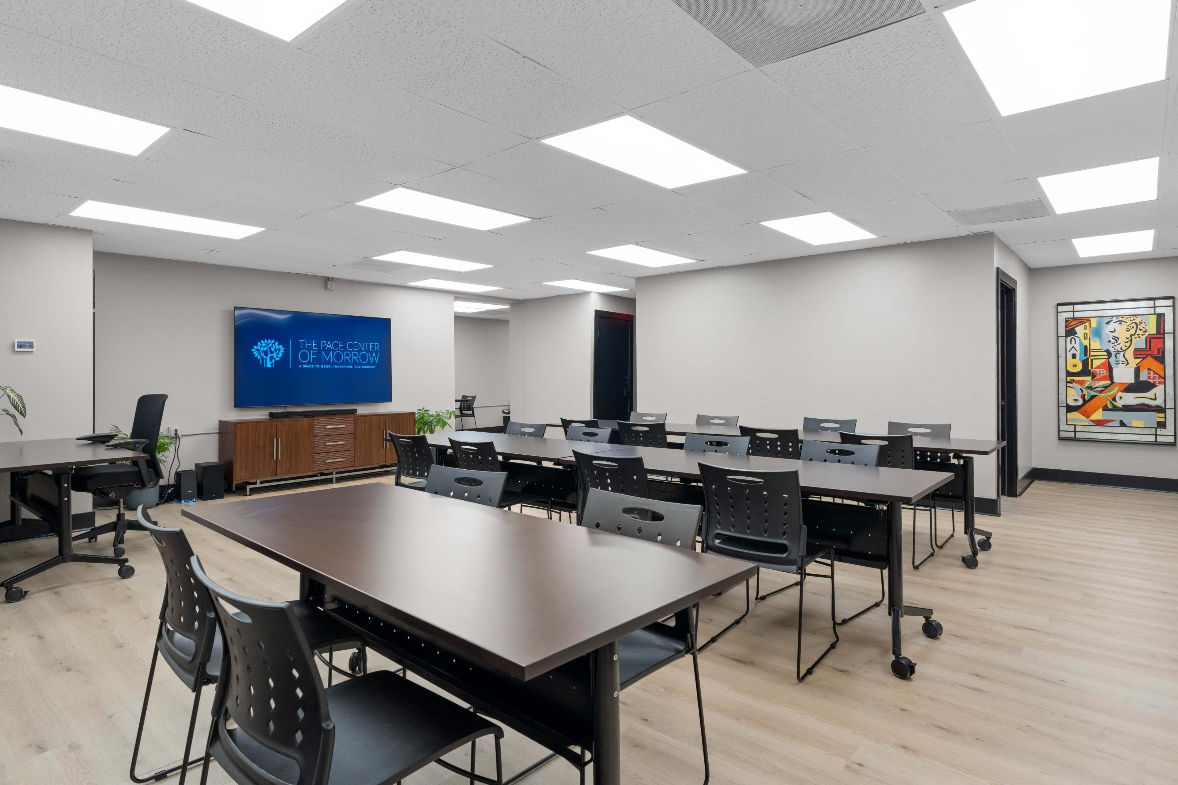A modern classroom setup with rows of tables and chairs, featuring a large screen displaying "The Pace Center of Morrow" on one wall.