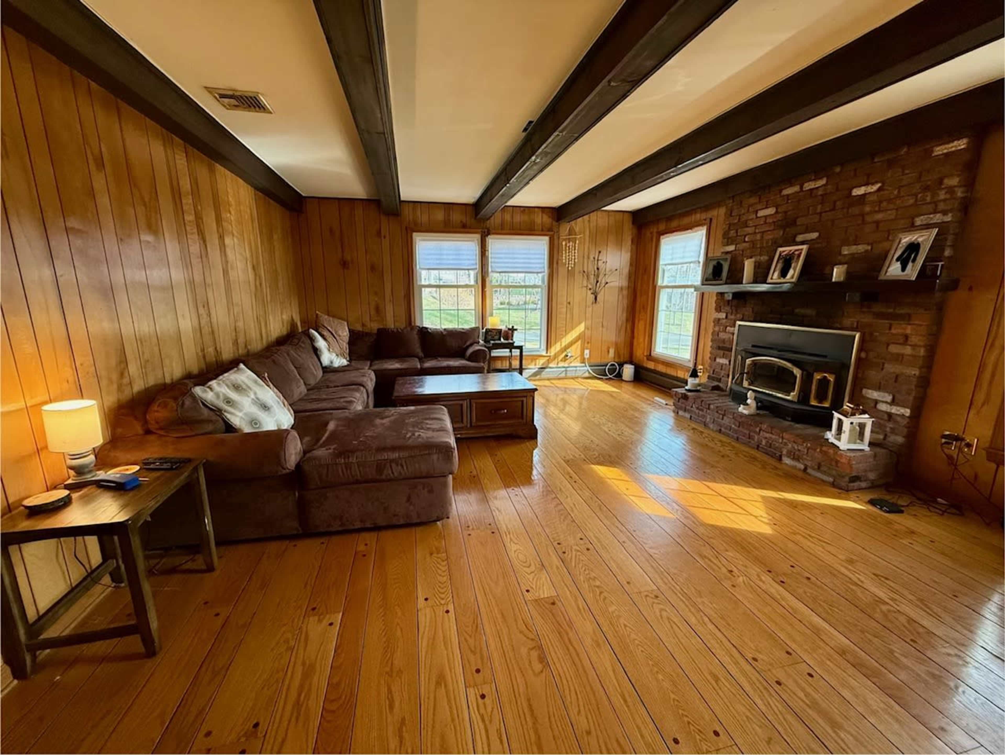 The image shows a spacious living room with wooden walls, a large sectional sofa, and a brick fireplace.