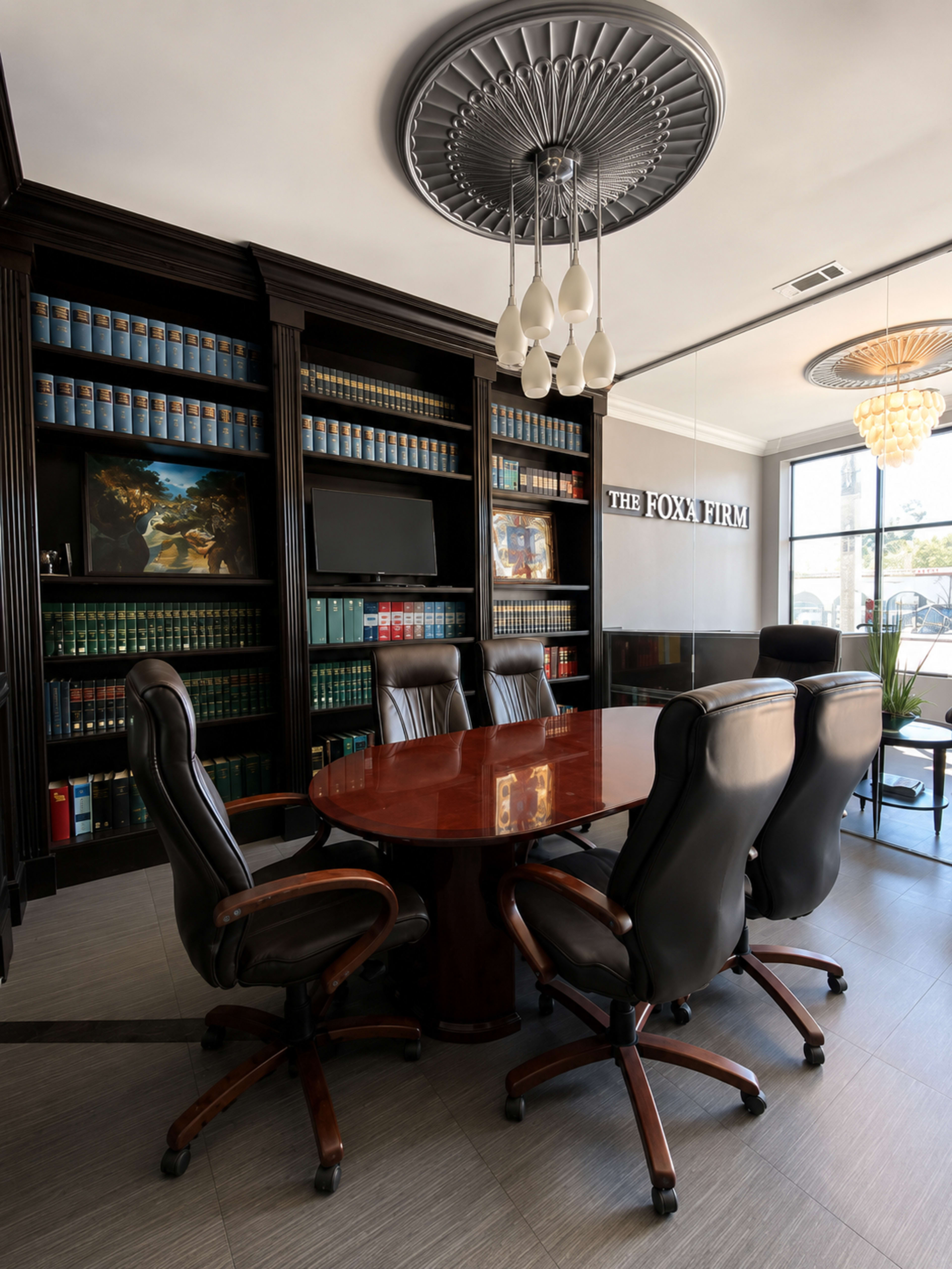 The image shows a modern conference room featuring a large round table surrounded by black leather office chairs, with a wall of bookshelves filled with books and decorative items.