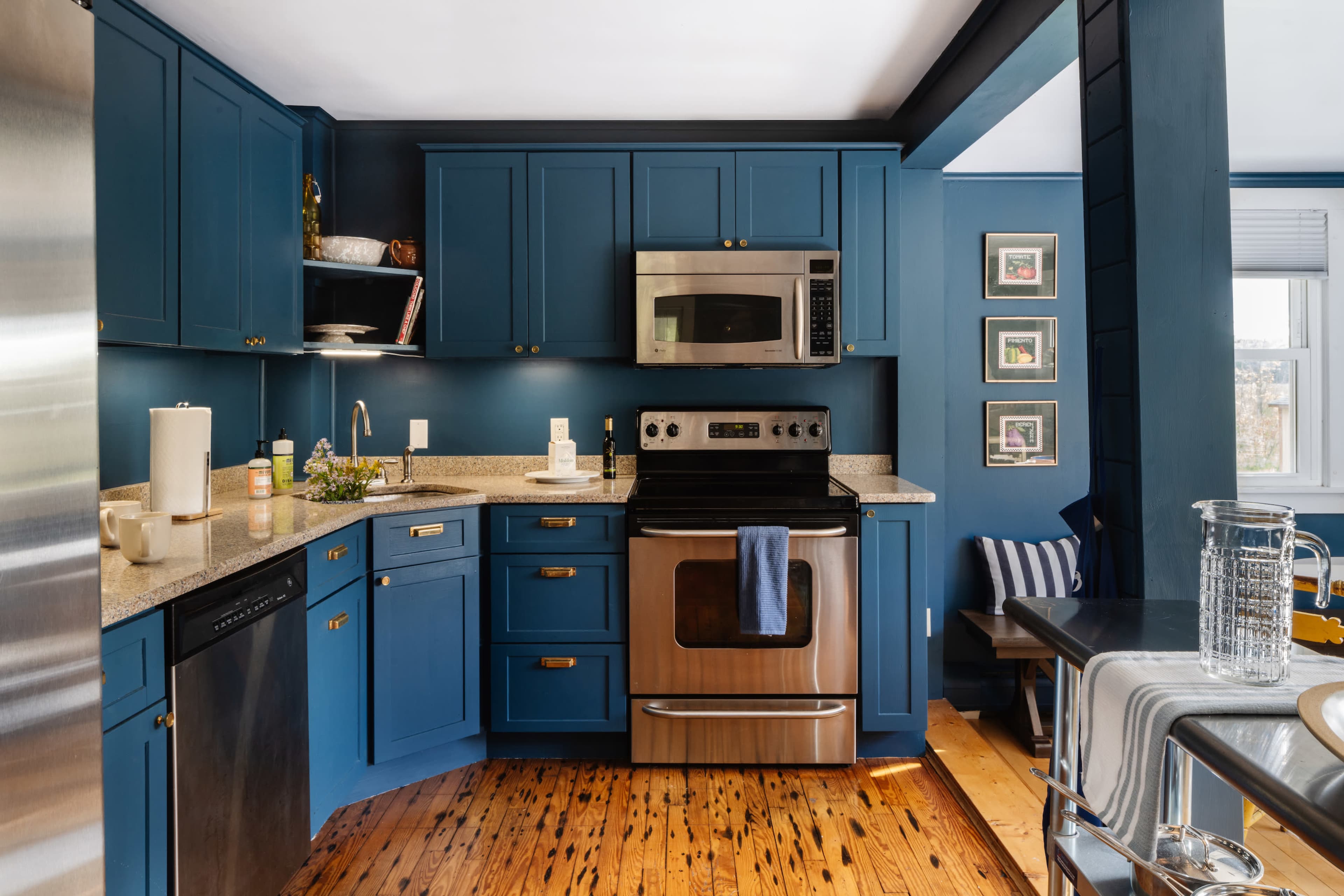 A modern kitchen with blue cabinets, stainless steel appliances, and wooden floors.