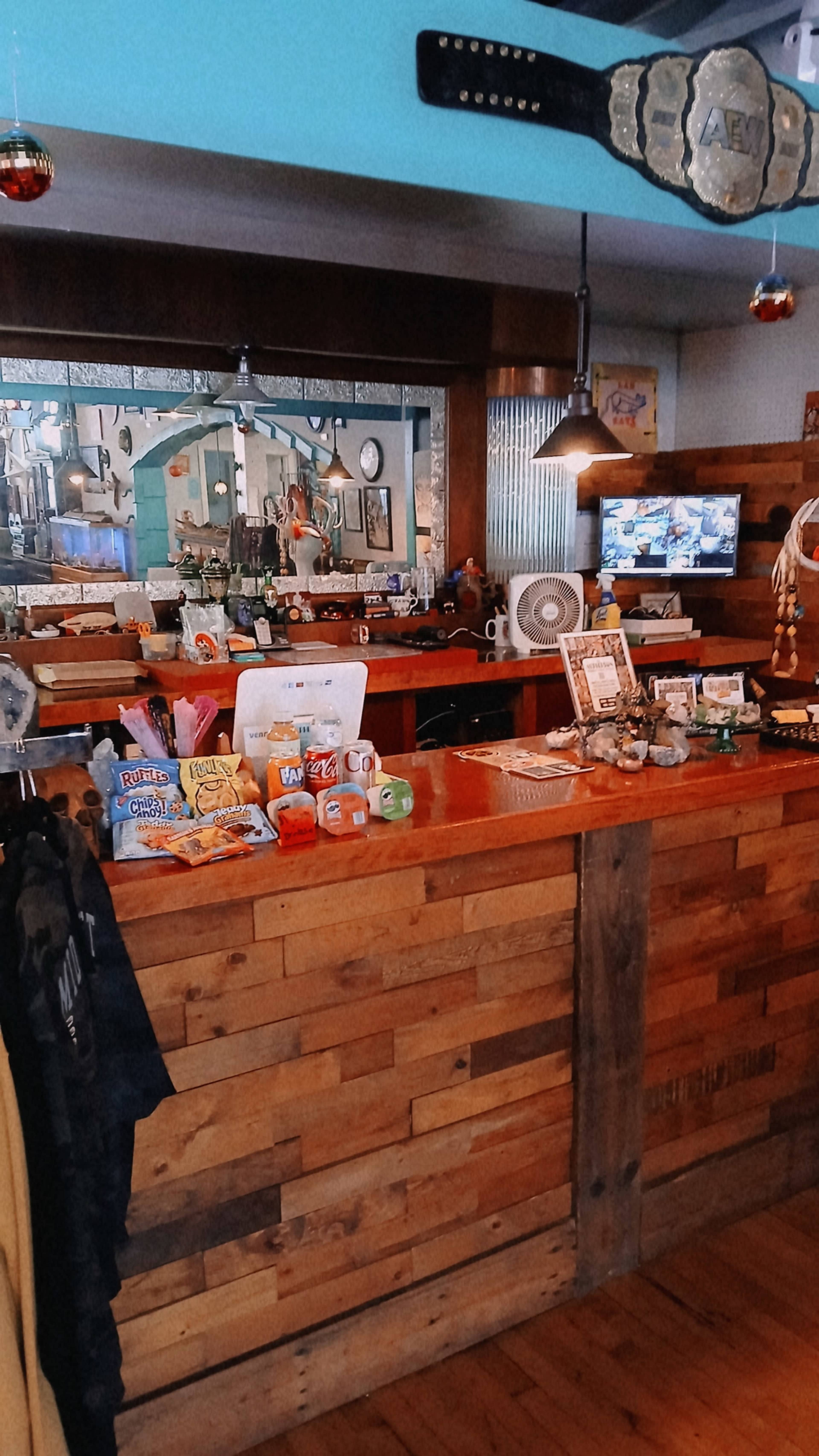 The image shows a cozy bar area with a wooden counter, displaying various snacks and drinks, and decorated with unique items, including a championship belt.