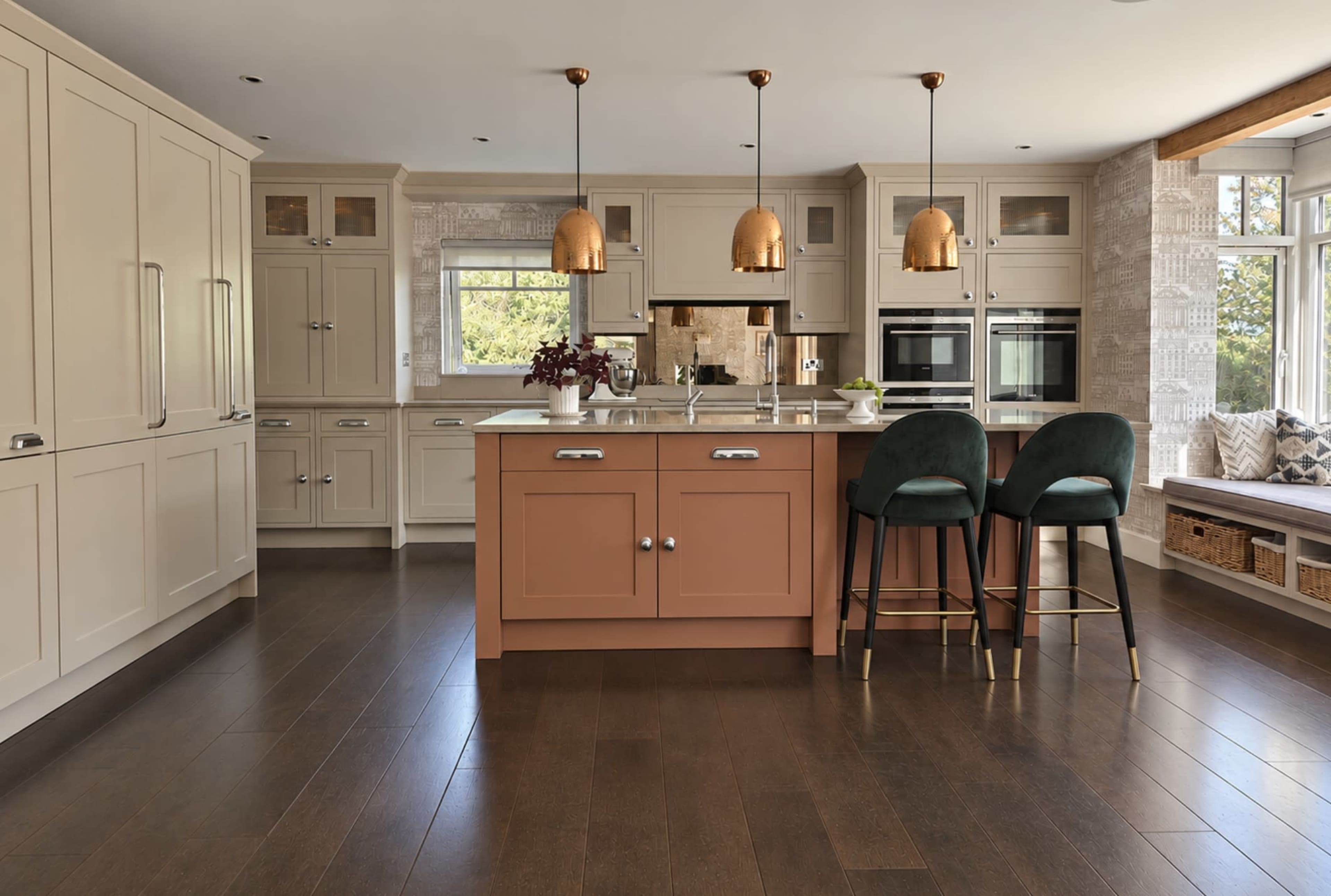 The kitchen features an island with a peach-colored base, paired with black stools and three copper pendant lights hanging above.