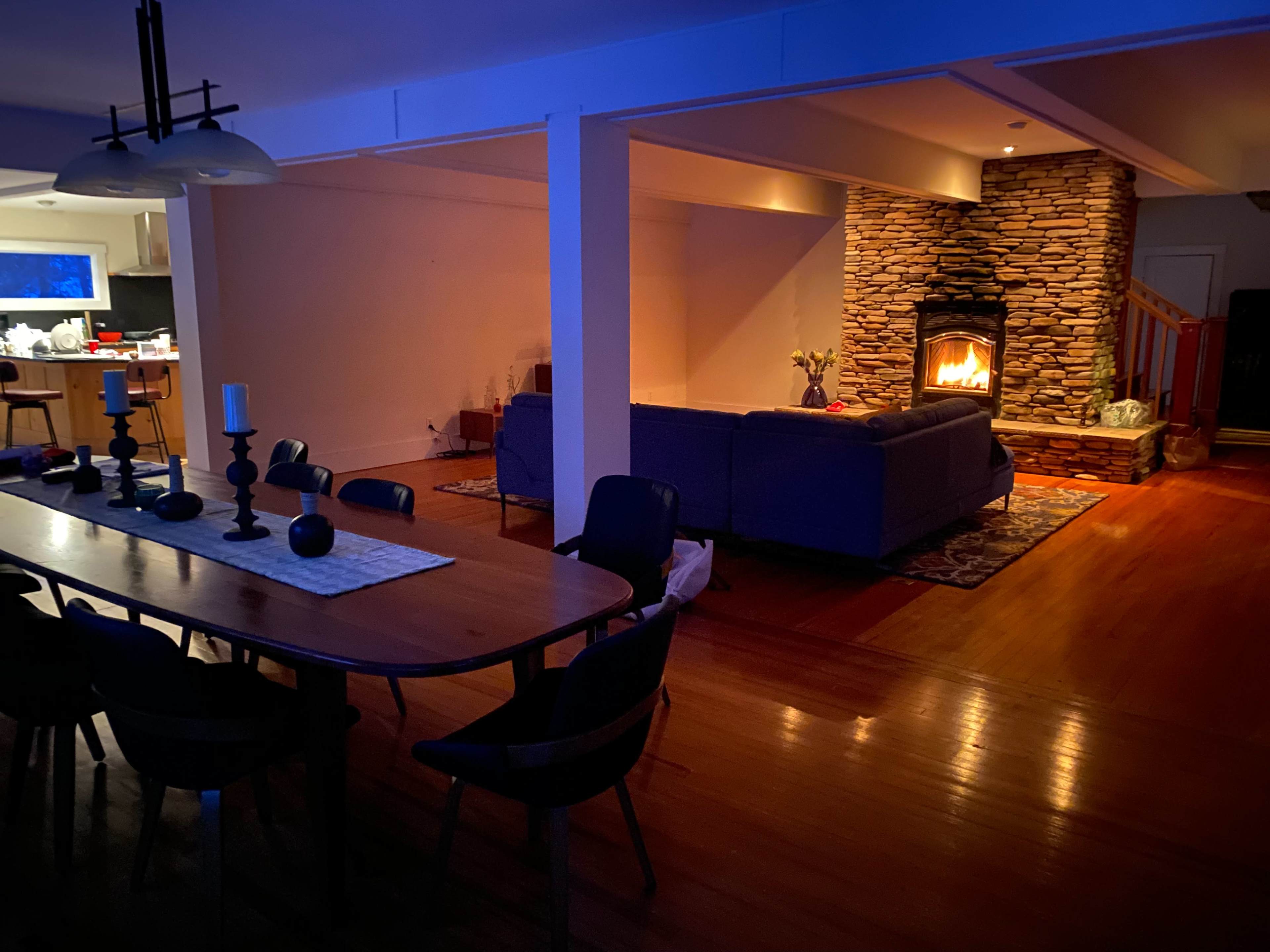 A dimly lit living space featuring a stone fireplace, a sectional sofa, and a dining table set for several people.
