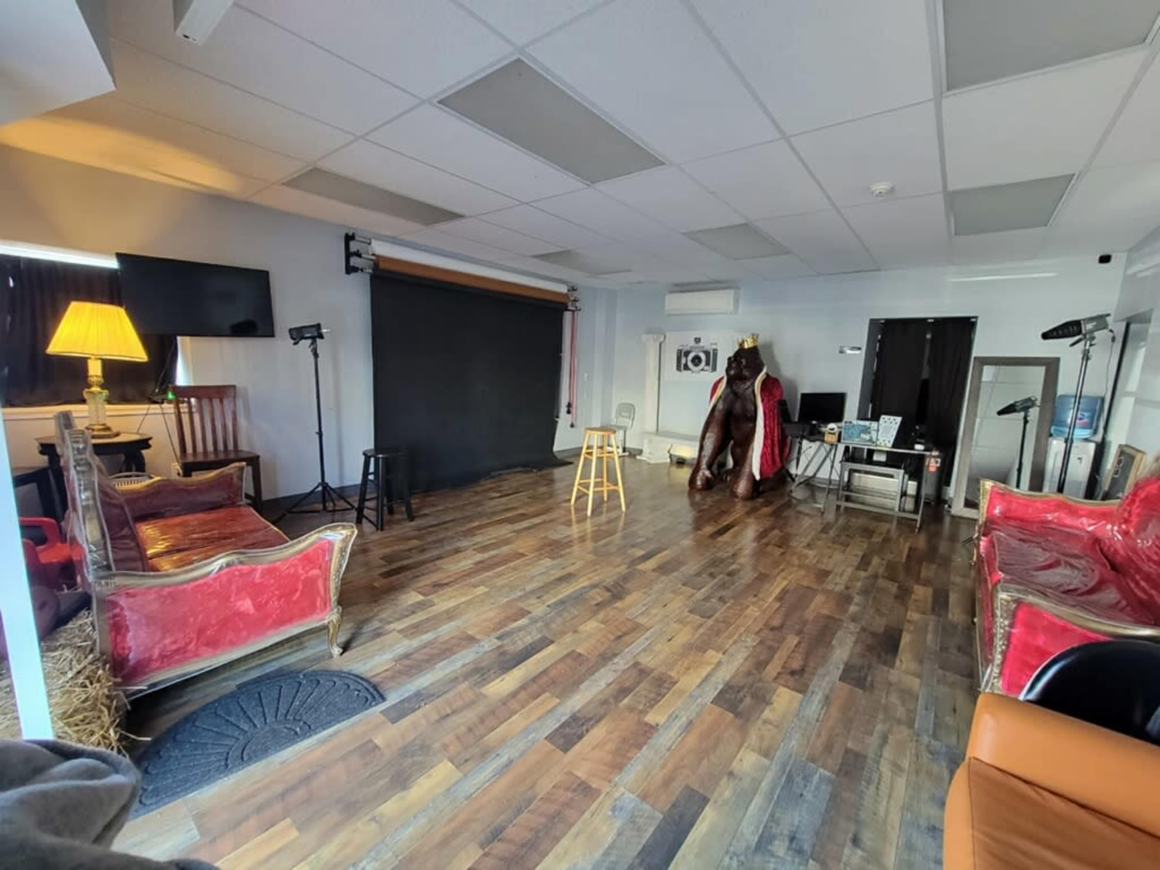 A spacious studio with wooden flooring, a black backdrop, a stool, several seating areas, and various equipment arranged around the room.