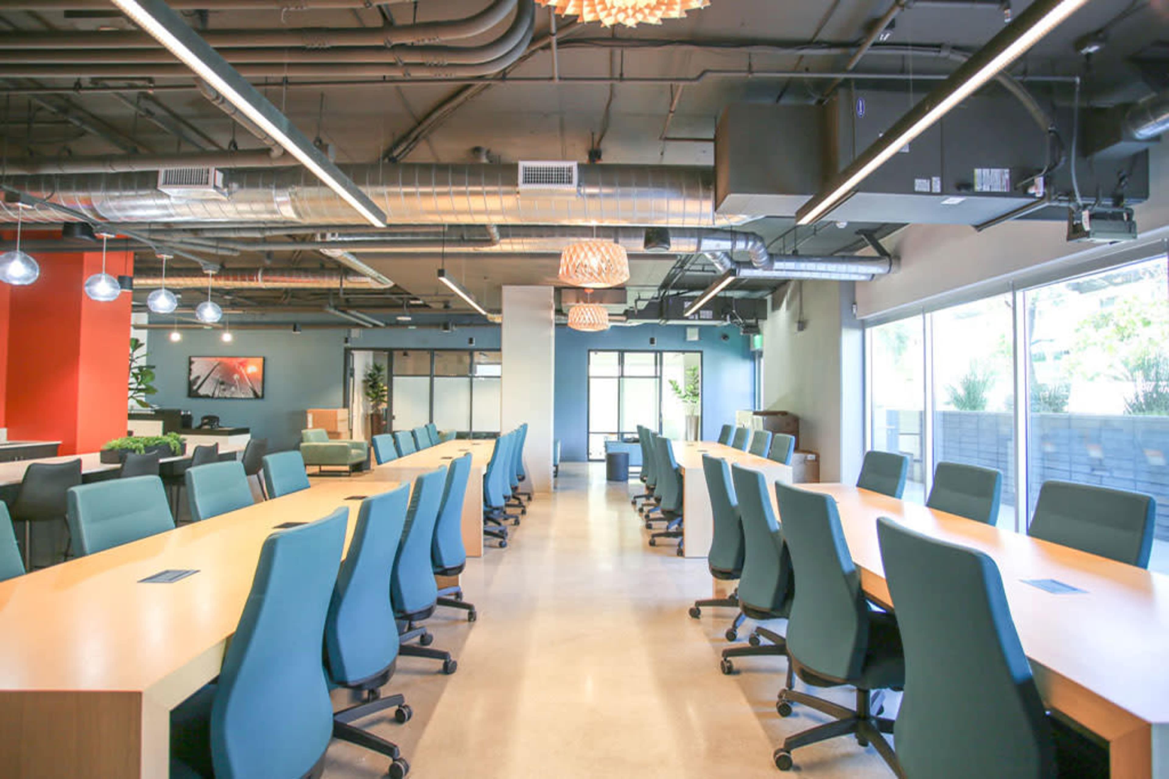 A modern office space with a long table and ergonomic chairs, surrounded by large windows and contemporary lighting fixtures.
