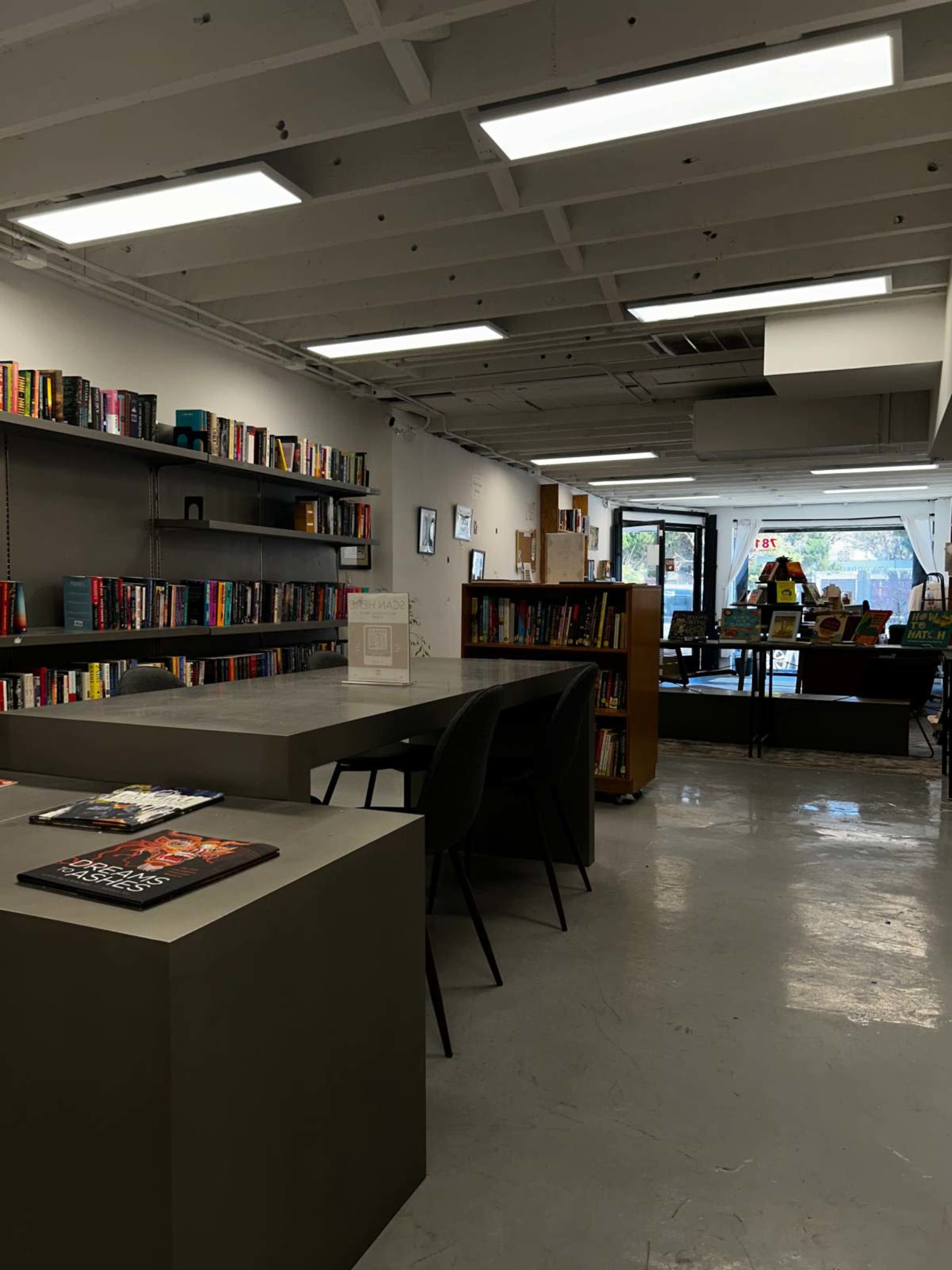 The image shows a modern library or bookstore interior with bookshelves lining the walls and a central table surrounded by chairs.