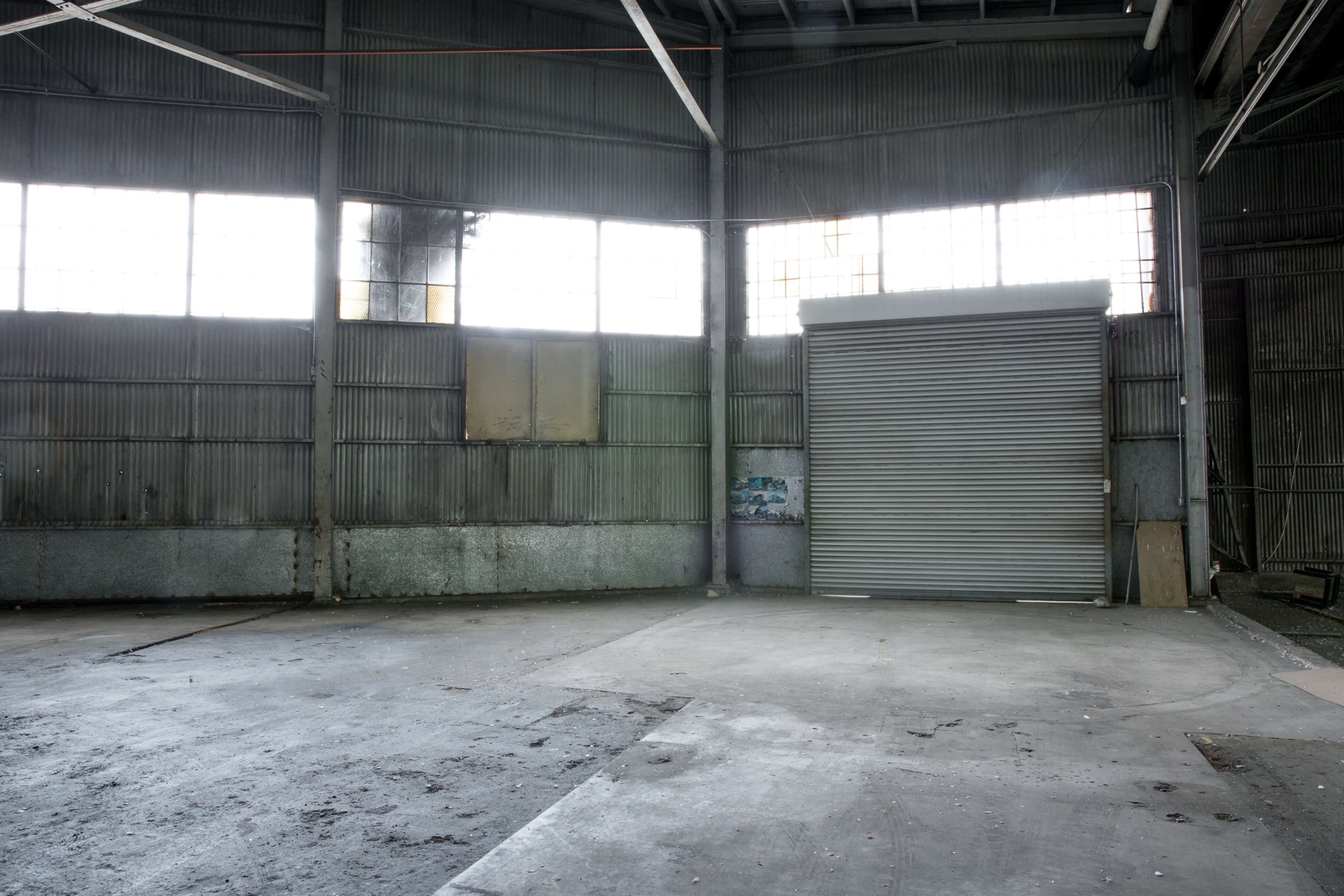 The interior of an empty industrial warehouse with large windows and a rolled-up metal door.