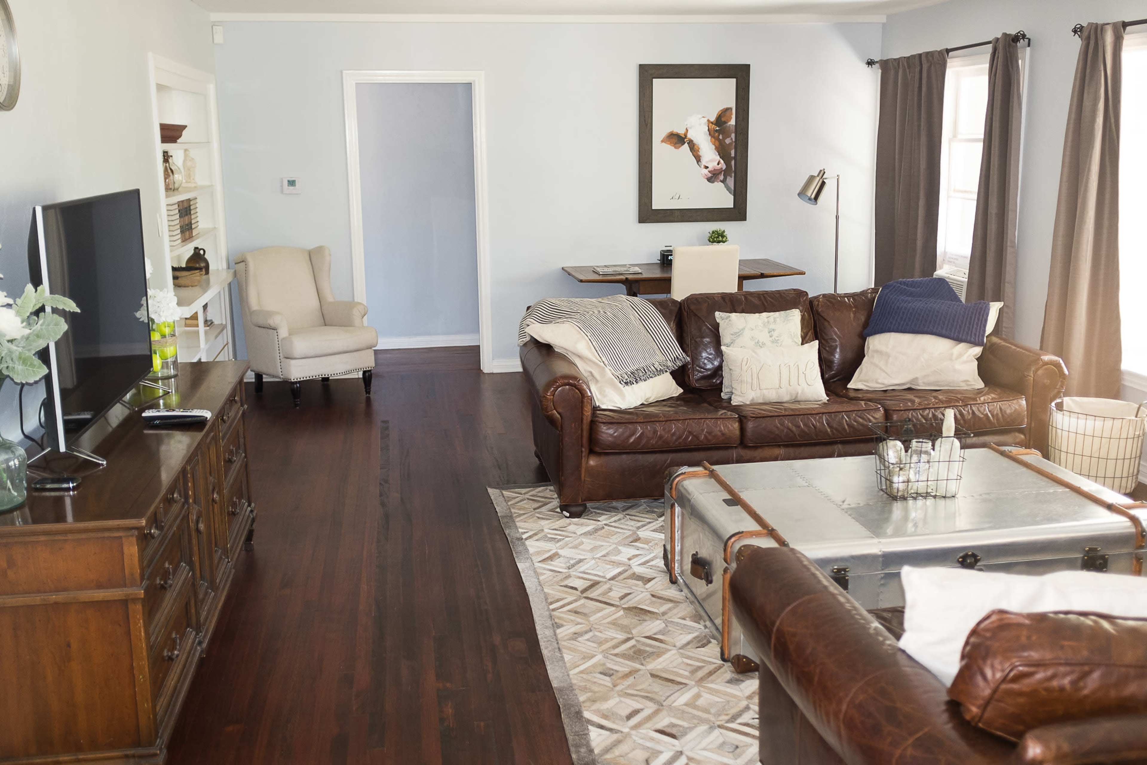 A cozy living room with brown leather sofas, a wooden television stand, and a framed artwork on the wall.