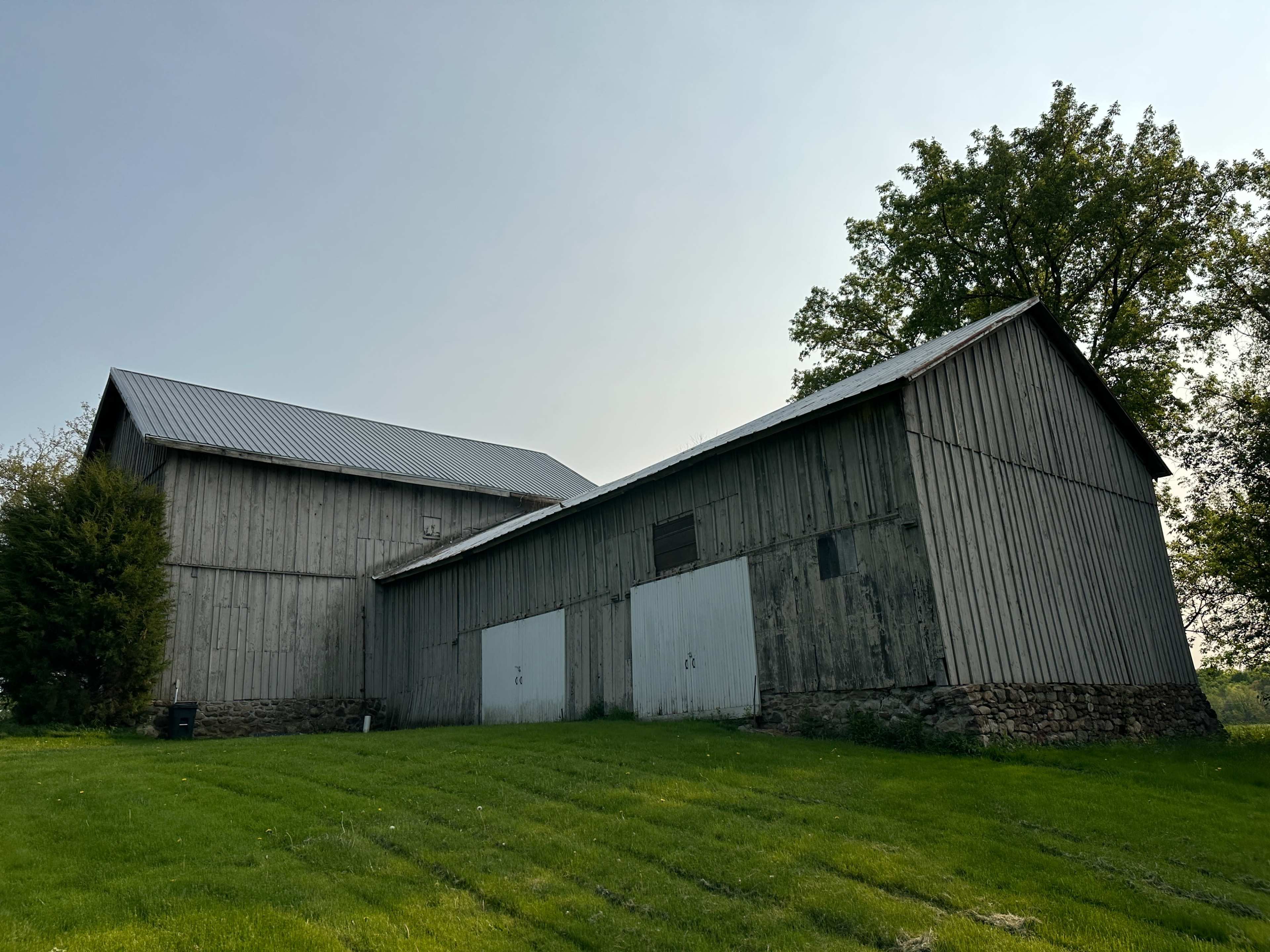 A weathered wooden barn with a metal roof stands beside a grassy area.