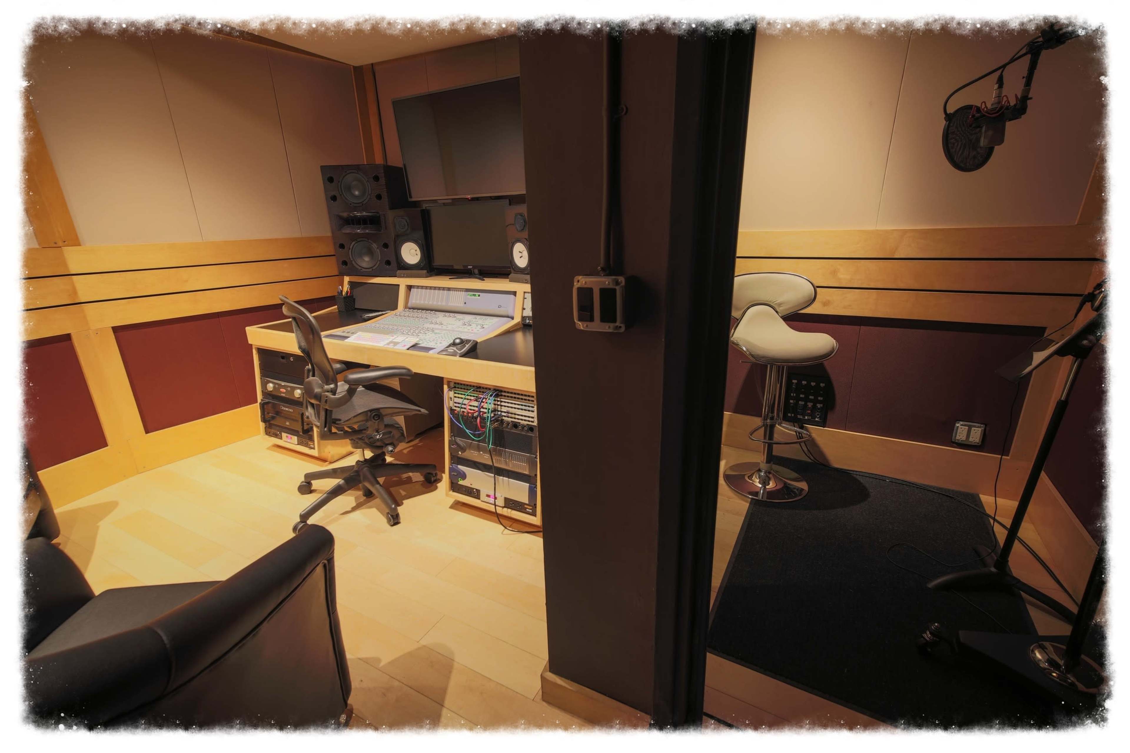 A recording studio with a sound mixing desk, a chair, and a separate vocal booth.