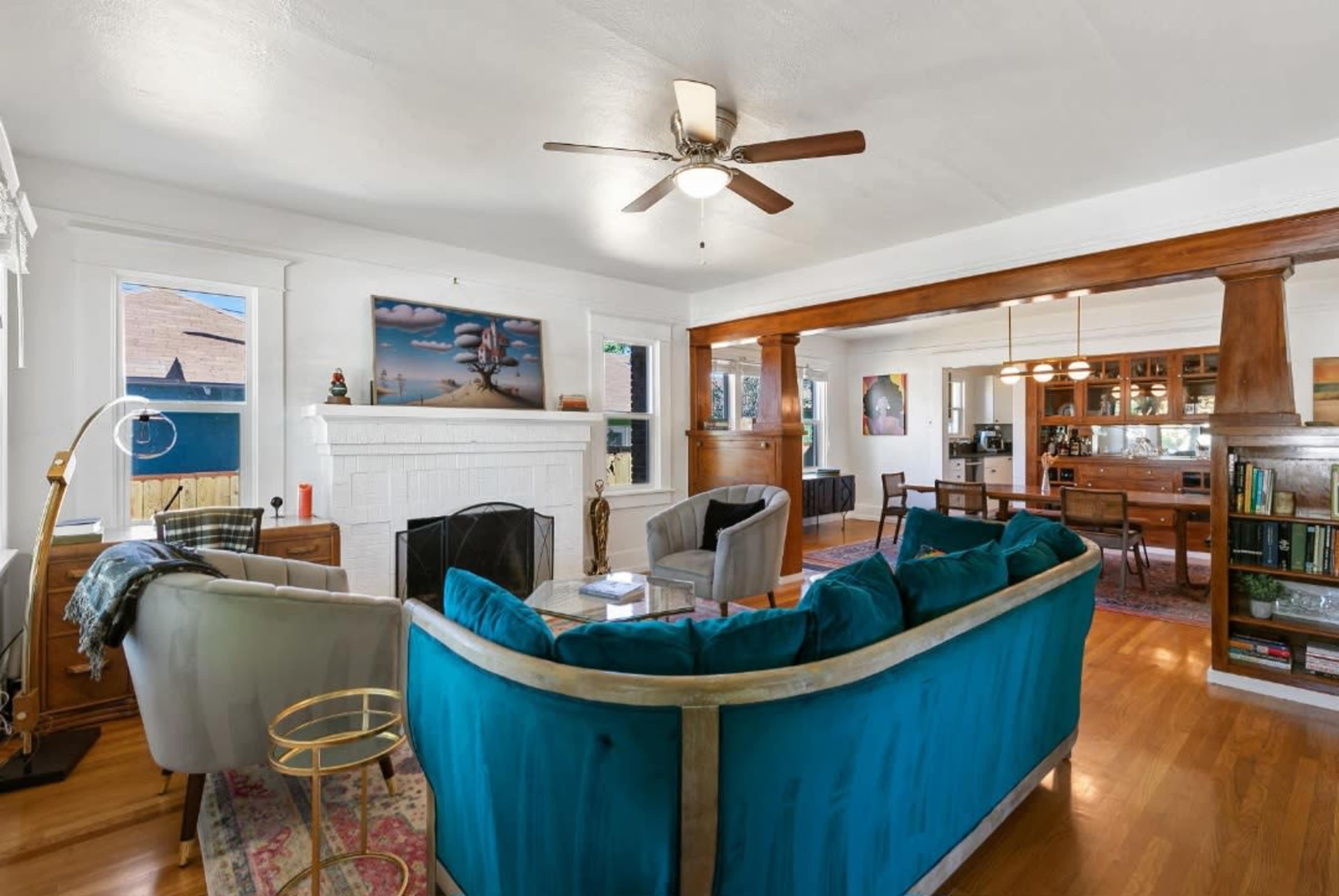 A living room features a turquoise sofa, wooden beams, and a fireplace, with a dining area visible in the background.