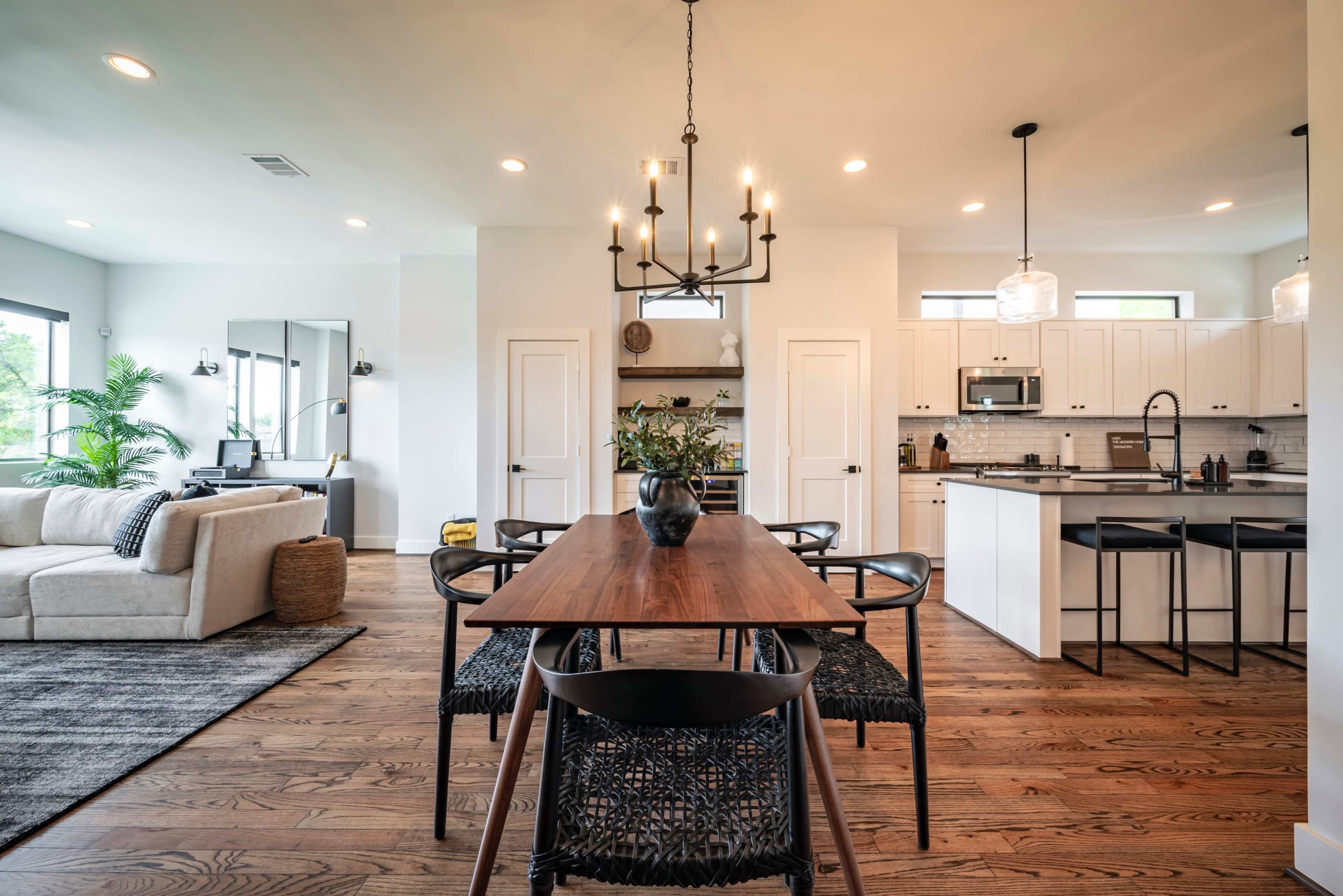 A modern dining area features a wooden table surrounded by chairs, with a view of an open kitchen and living space adorned with natural light.