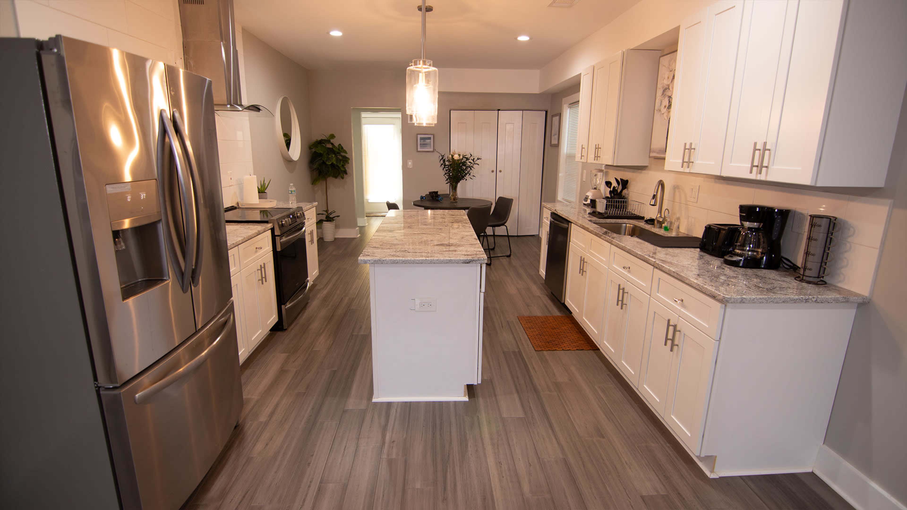 A modern kitchen features stainless steel appliances, white cabinetry, and a central island with a gray countertop.