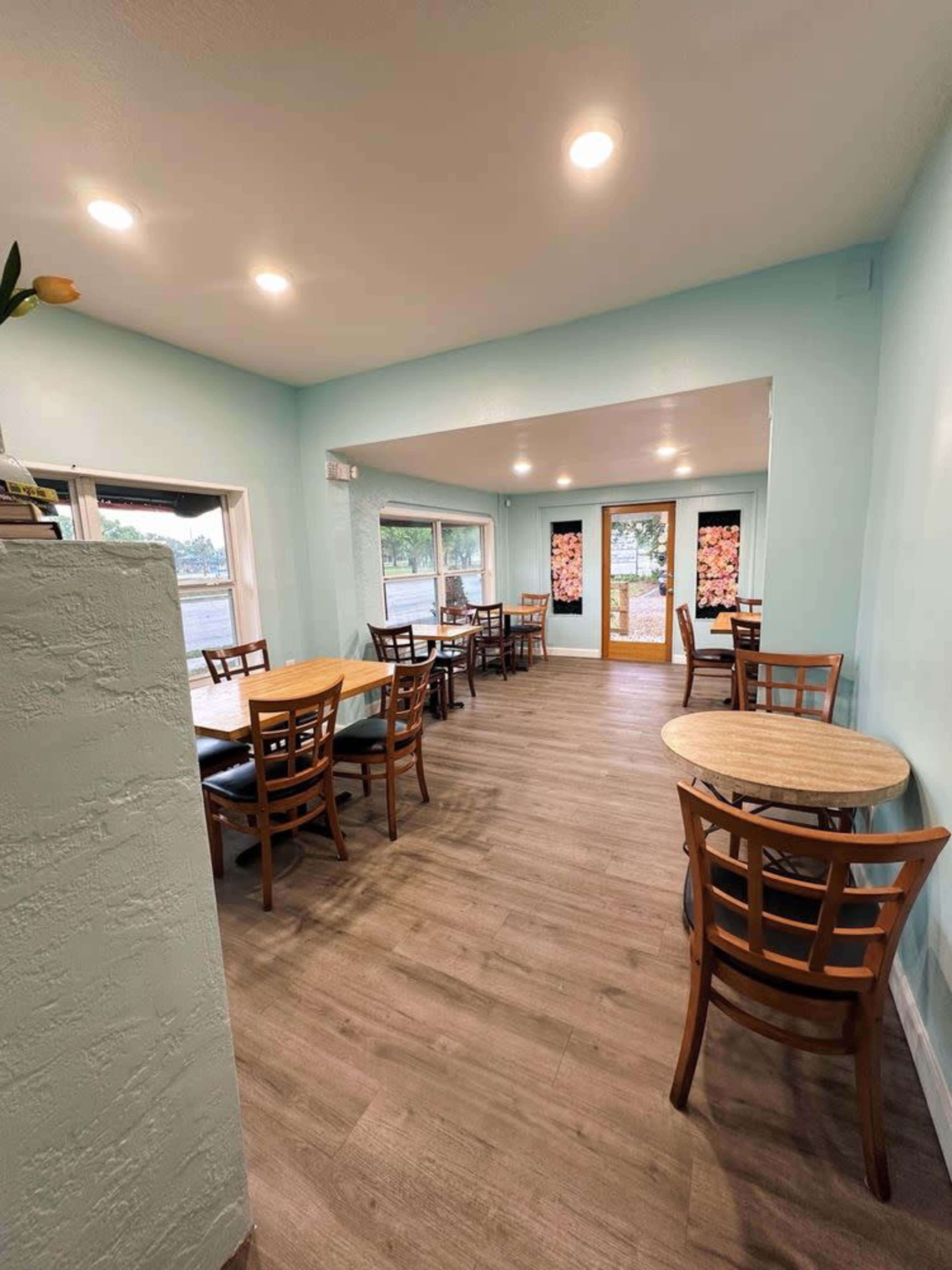The image shows a light blue-walled café interior with wooden tables and chairs arranged neatly along the walls.