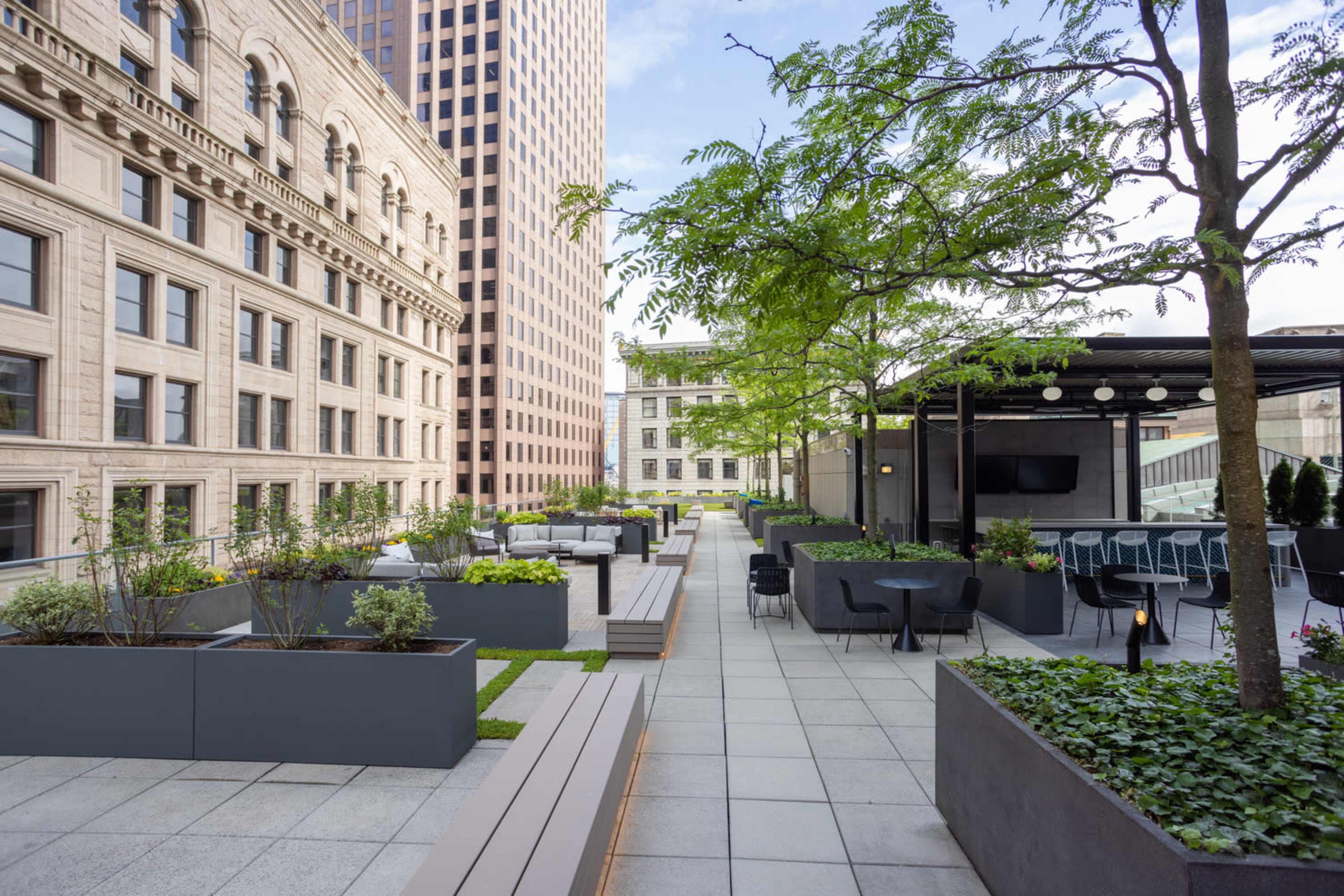 A landscaped rooftop terrace with modern seating areas, planters, and a view of adjacent buildings.