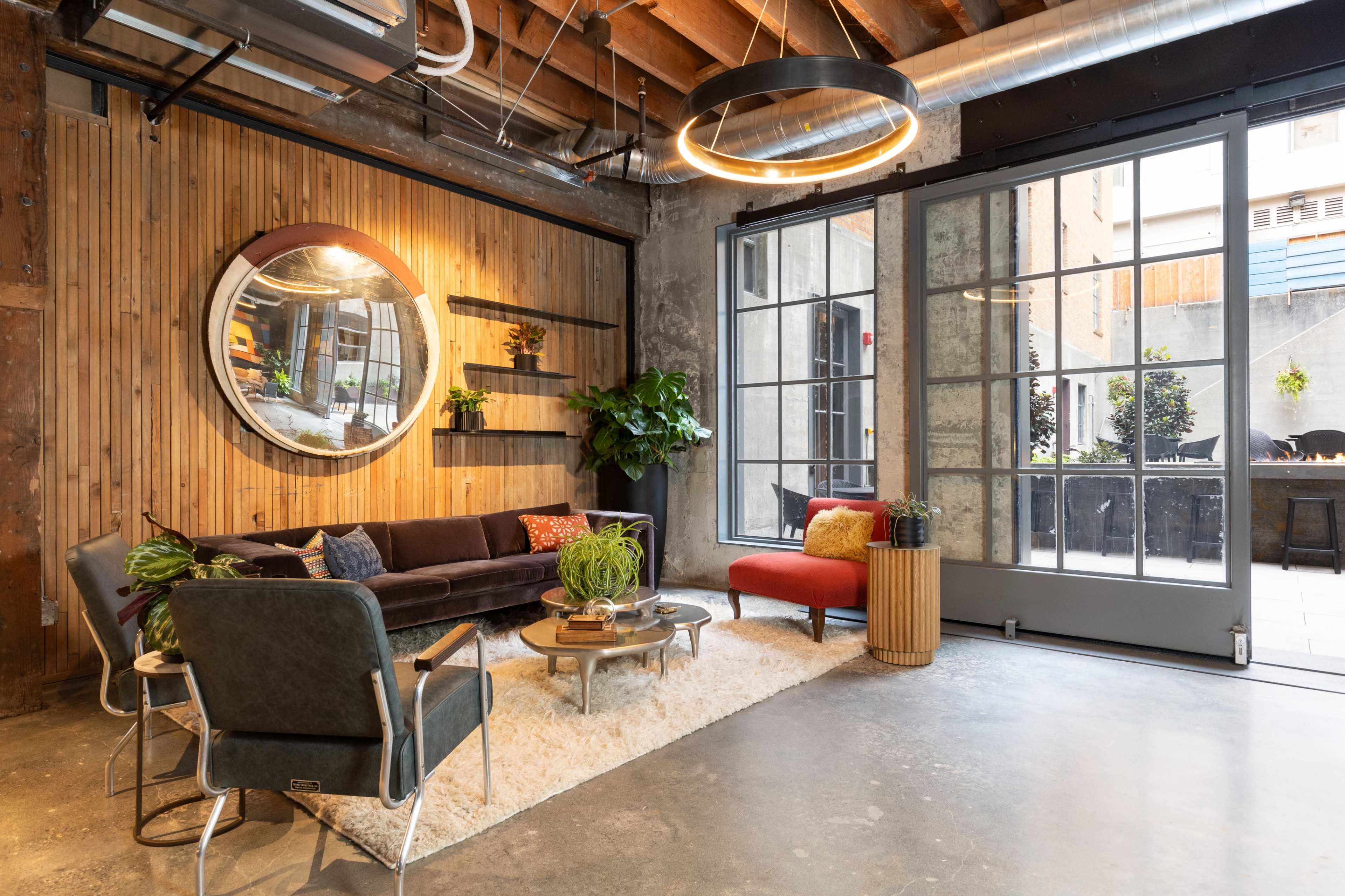 A modern lounge area with a wooden accent wall, a round mirror, a comfortable seating arrangement, and large windows leading to an outdoor space.