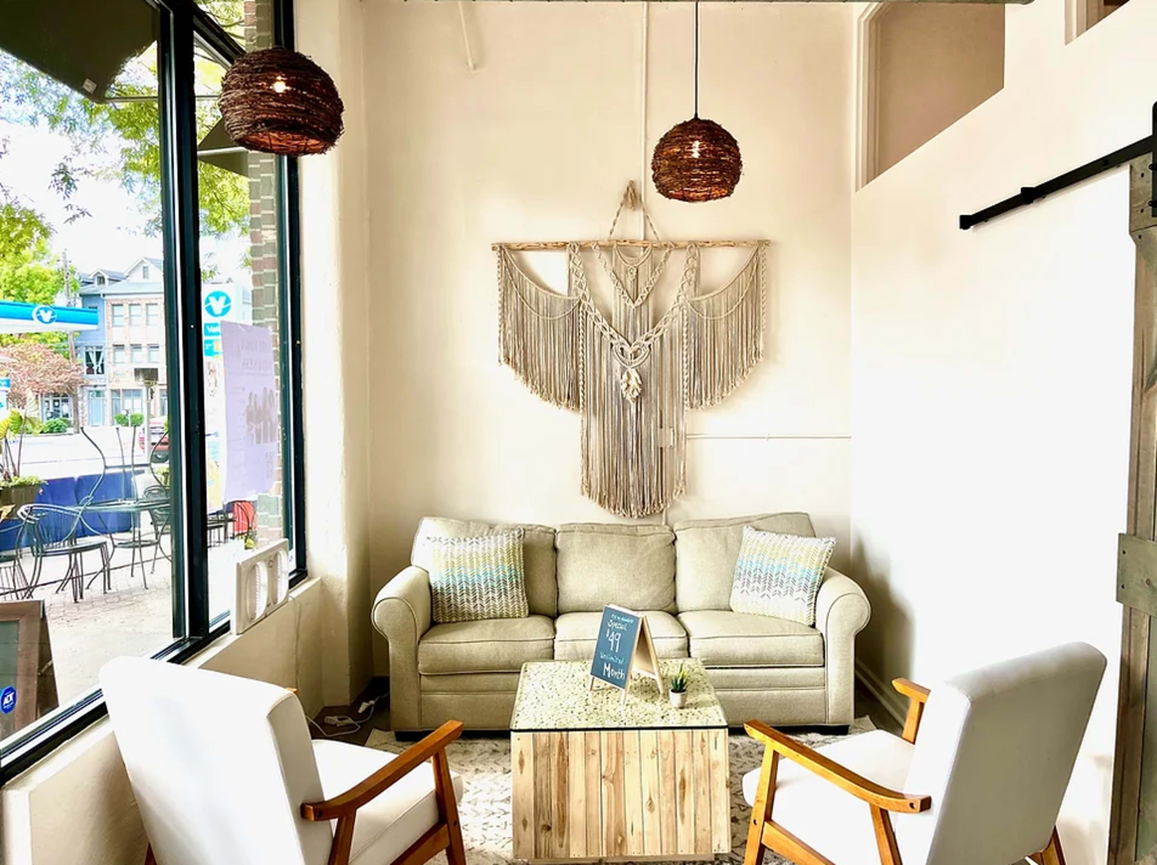 A cozy sitting area with a light gray sofa, two white chairs, and a wooden coffee table, adorned with a macramé wall hanging.