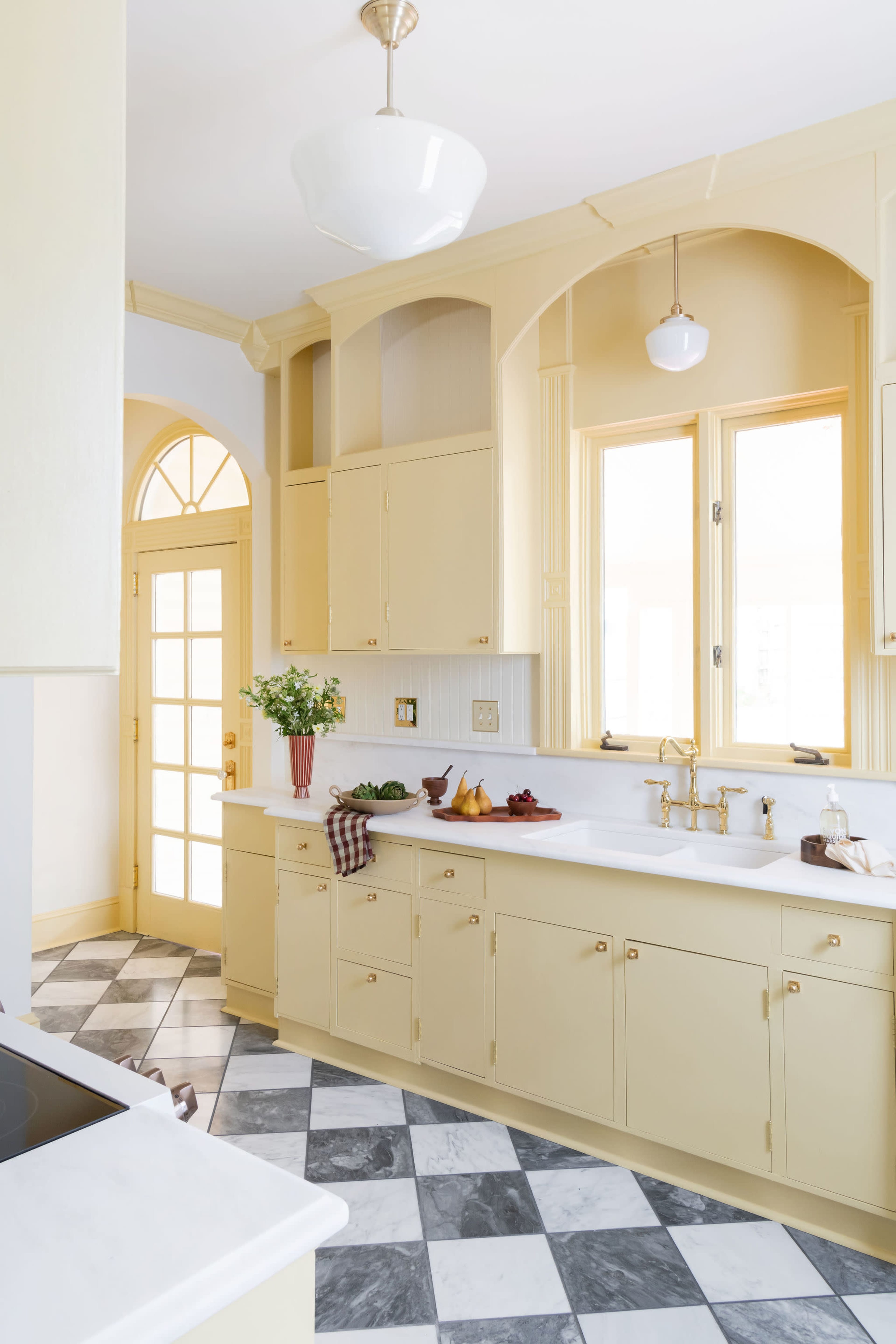 The kitchen features yellow cabinetry, a marble countertop, and a checkered floor with large windows allowing natural light to enter.