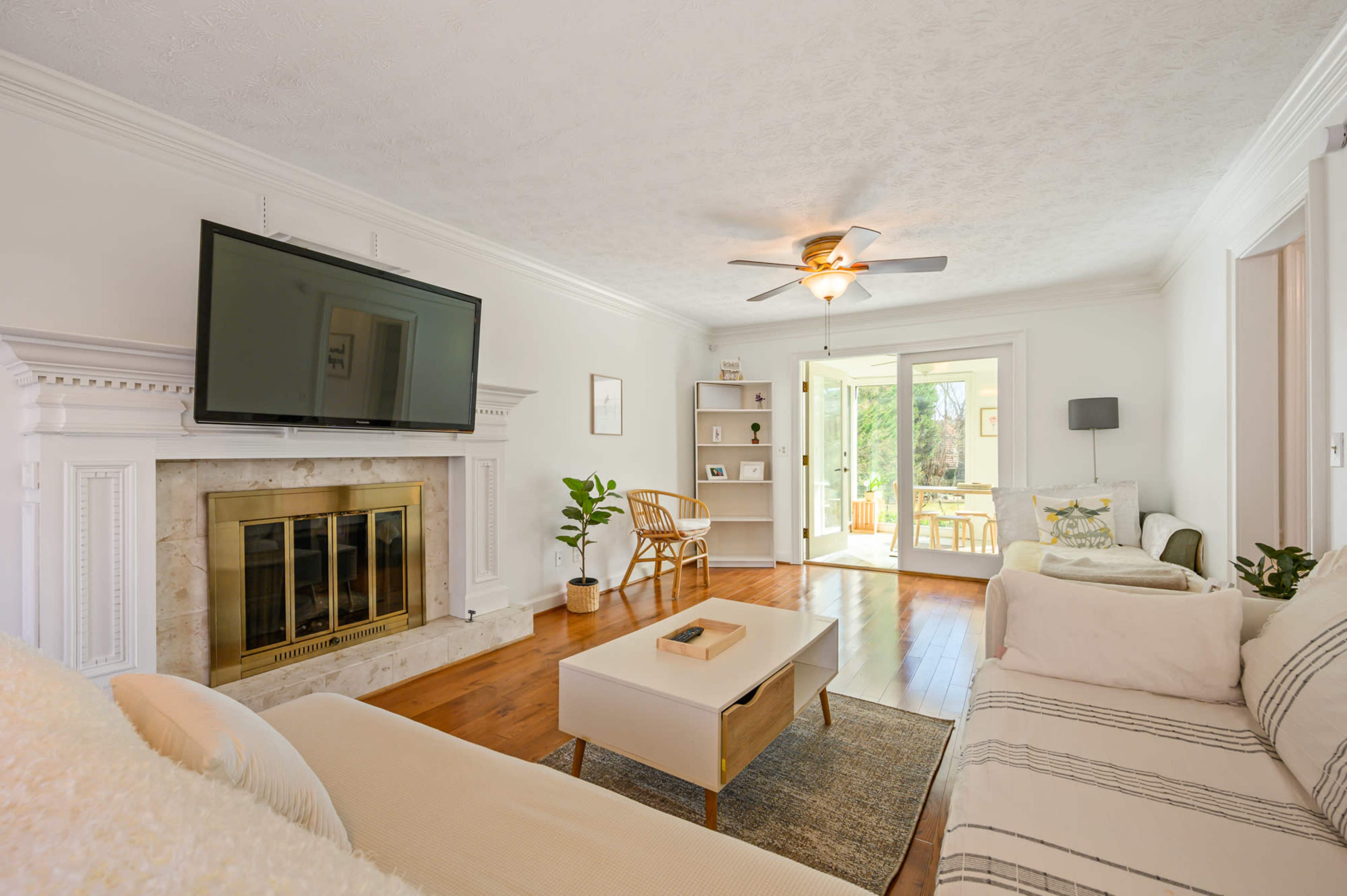 A modern living room features a large television mounted above a fireplace, a coffee table, two couches, and doors leading to a patio.