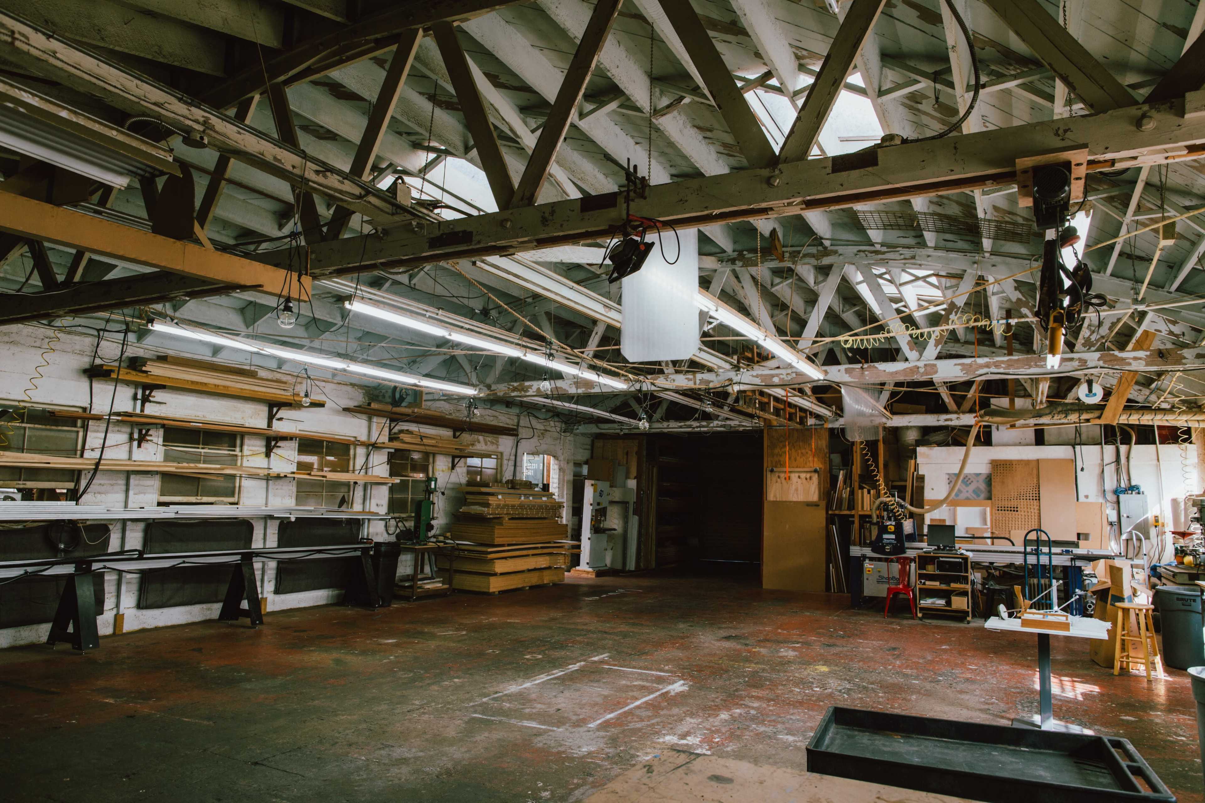 A spacious workshop with wooden beams, large worktables, and various tools and materials organized along the walls.