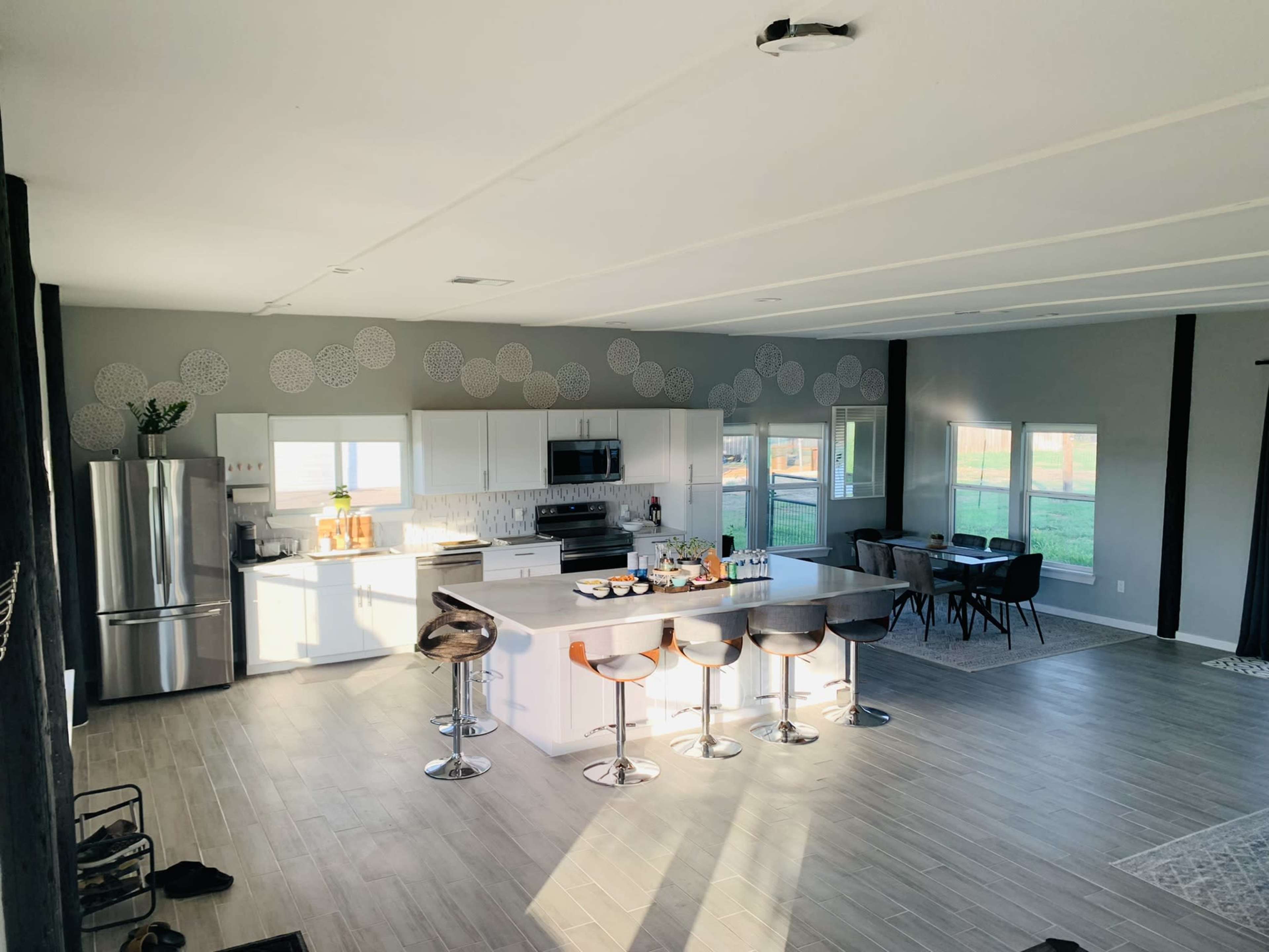 A spacious modern kitchen features a large island with seating and stainless steel appliances, adjacent to a dining area with a view of the outdoors.