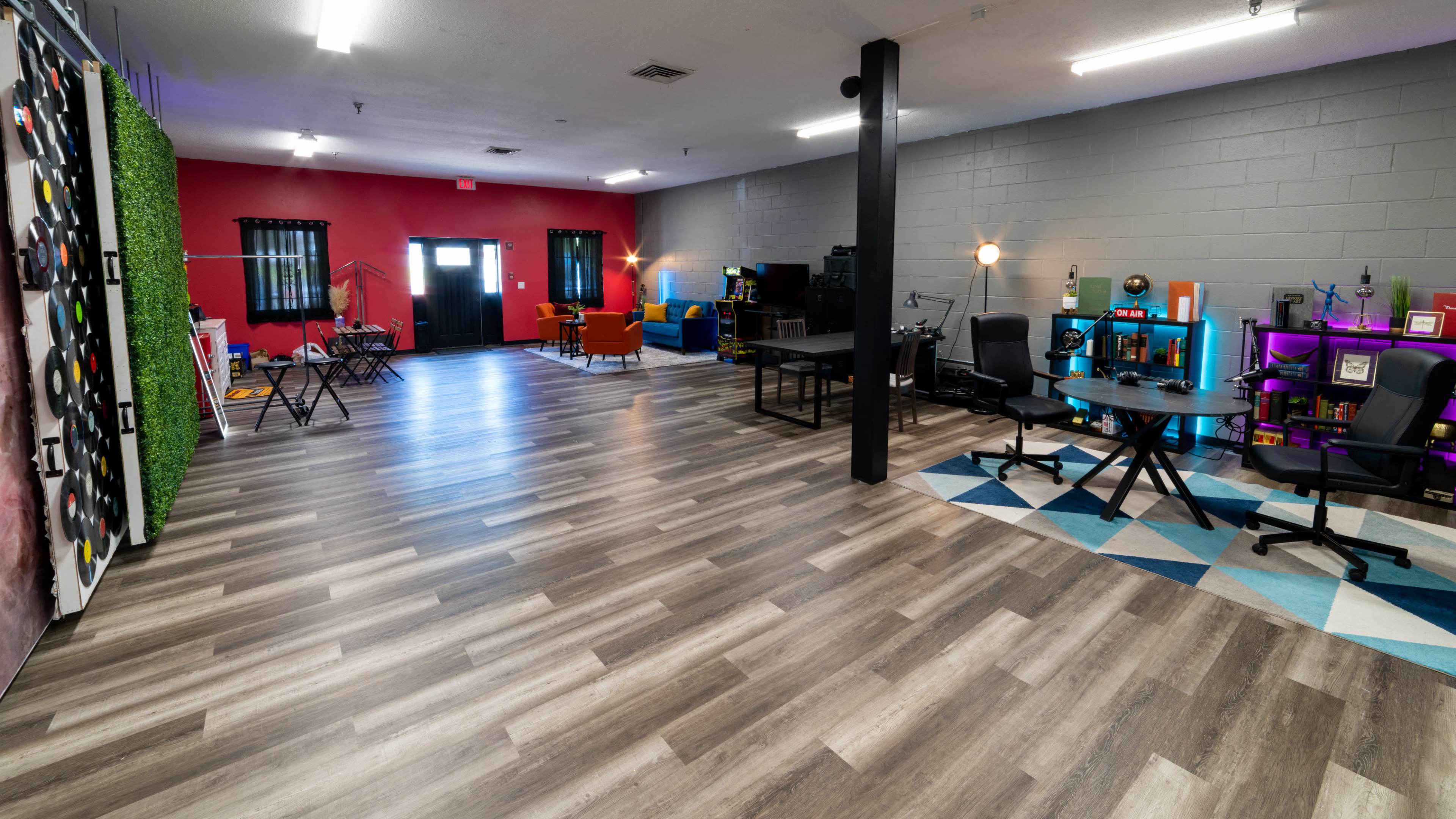 A spacious room with a polished wooden floor, featuring various seating areas and workstations, along with colorful decor against the walls.