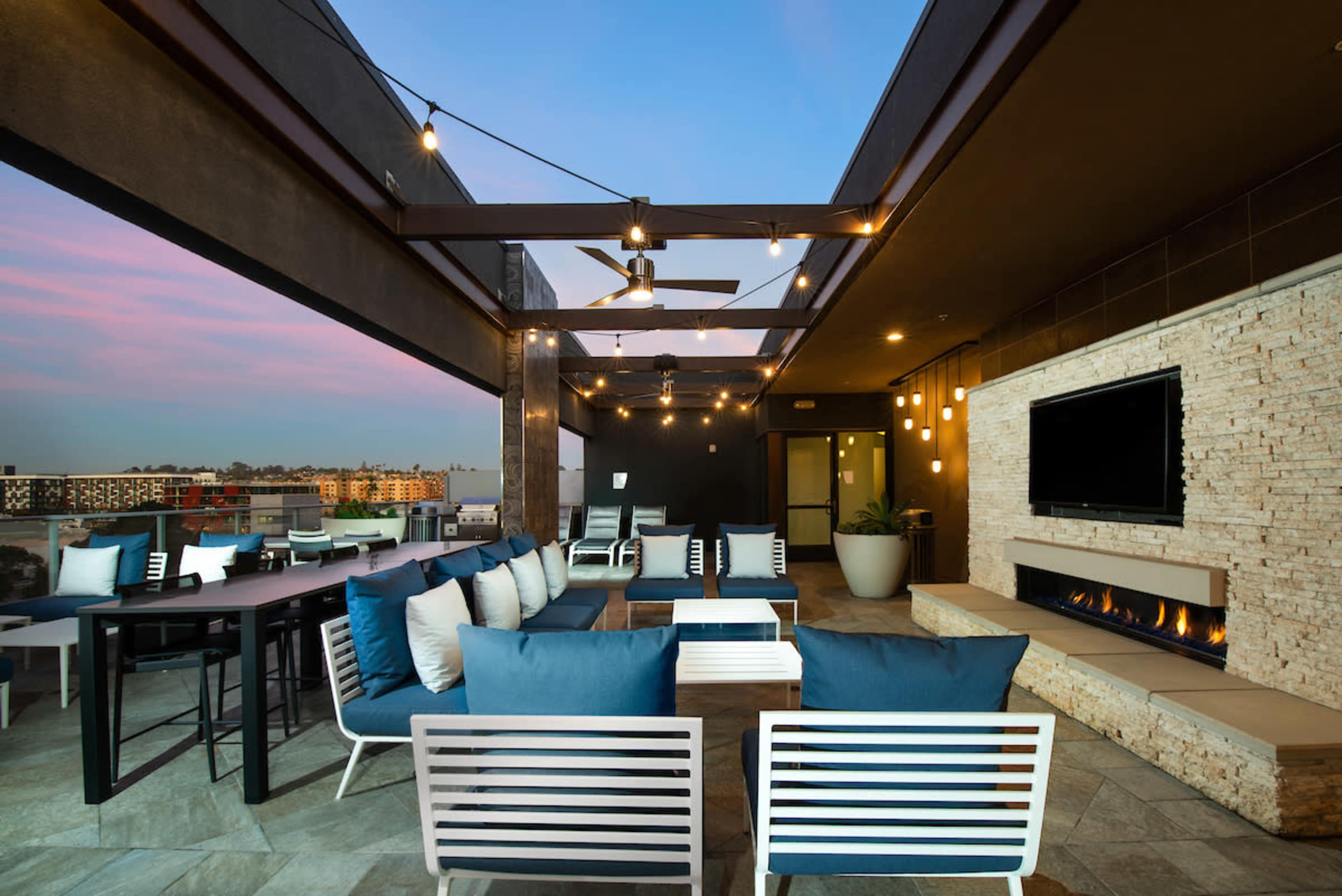 A modern rooftop lounge area with comfortable seating, a television, and decorative lighting.