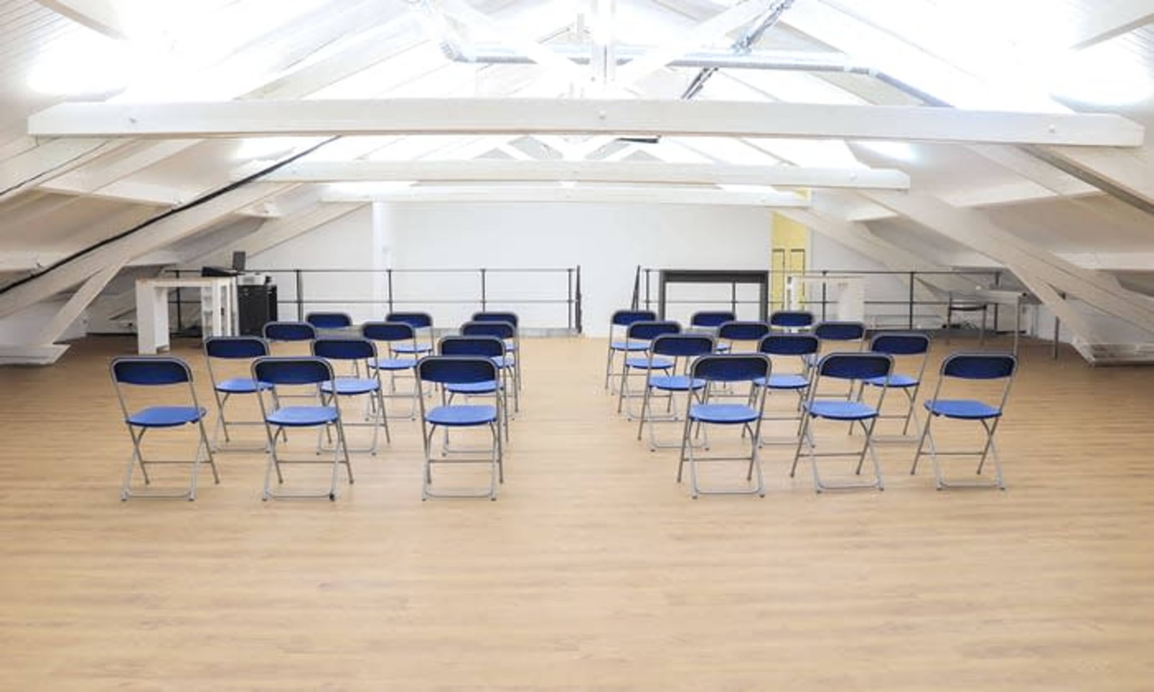 The image shows a spacious, well-lit attic with rows of blue folding chairs arranged for an event.