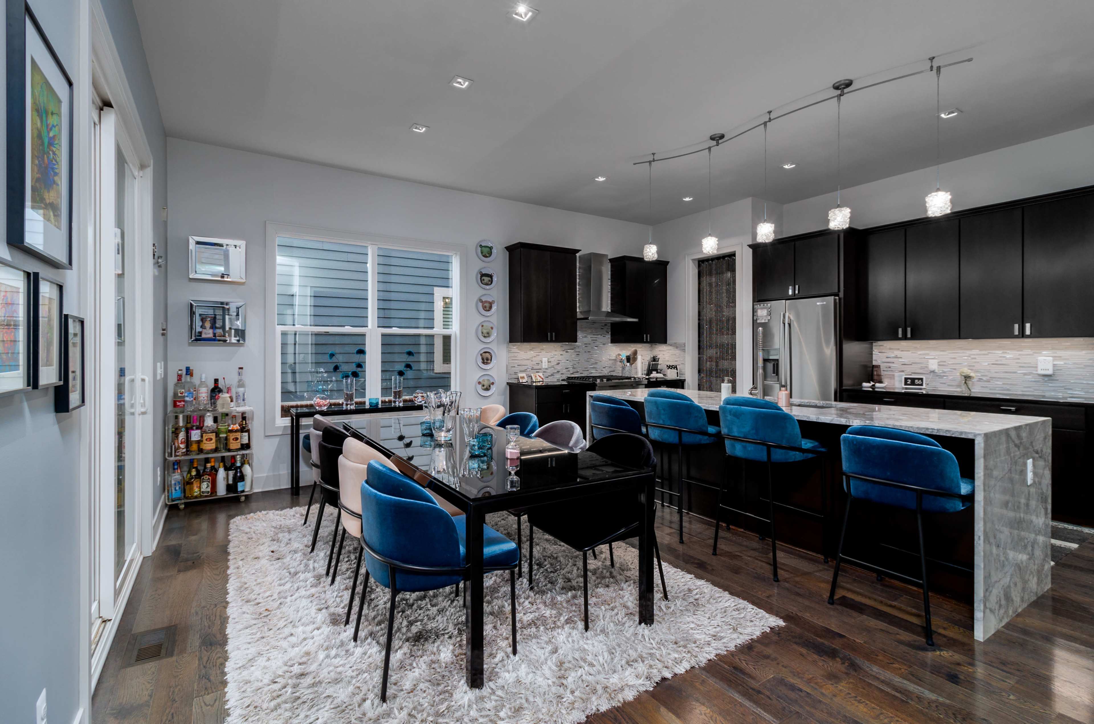 A modern kitchen and dining area features a large table with eight chairs, a sleek bar counter with stools, and stylish cabinetry.