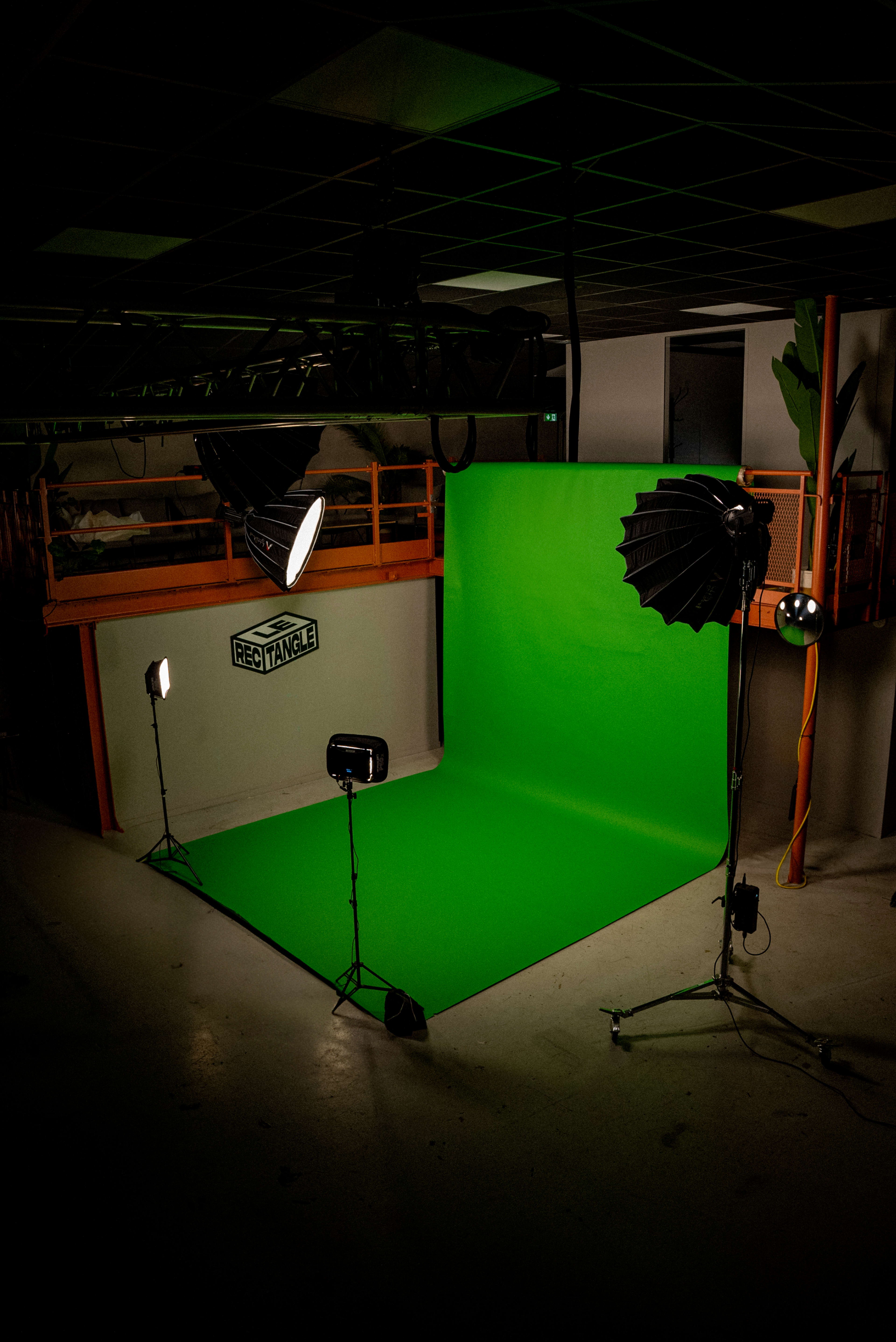 A photography studio with a green backdrop and various lighting equipment set up.