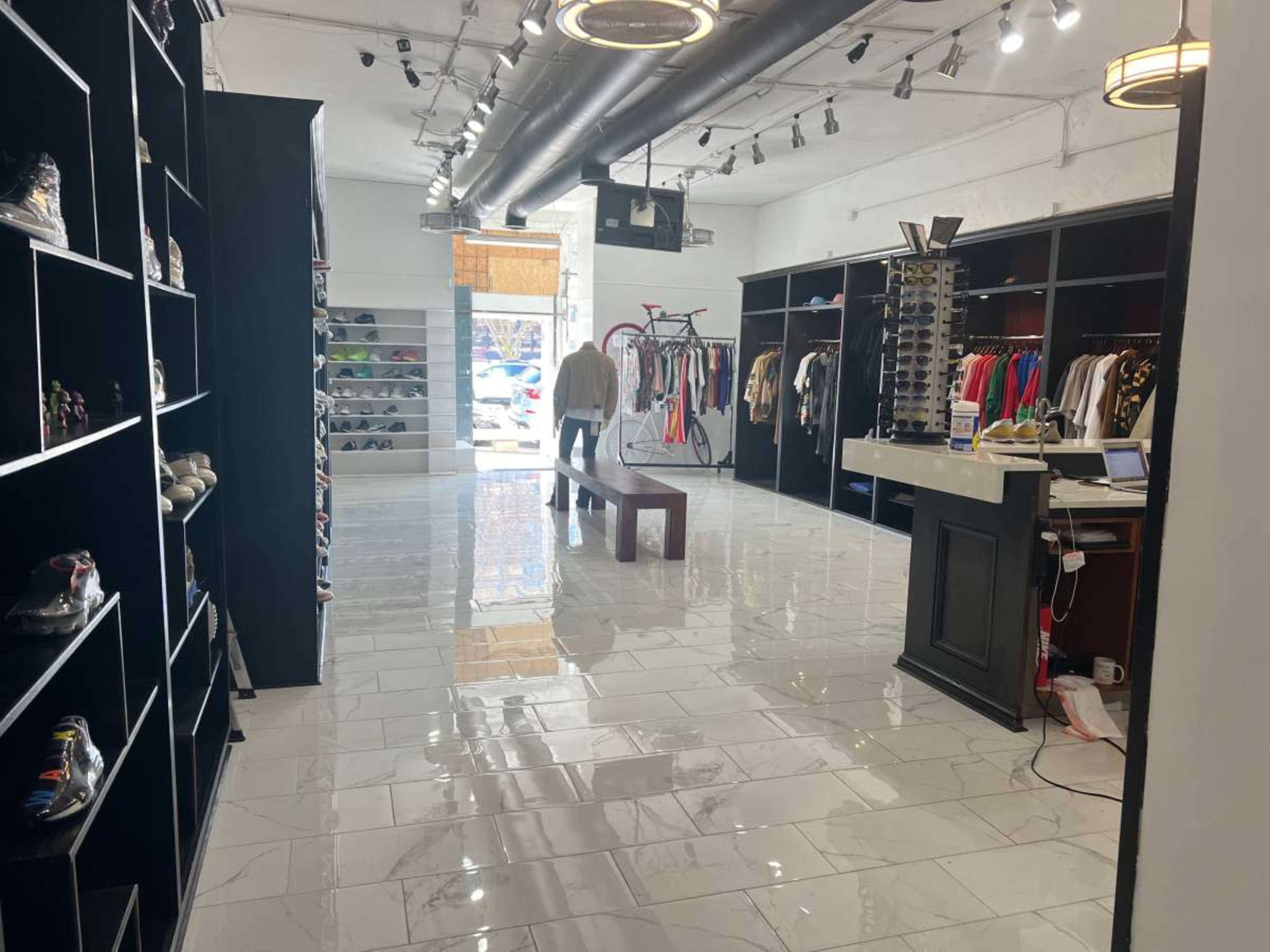 The image shows a retail store interior featuring display shelves filled with clothing and shoes, along with a central seating area.